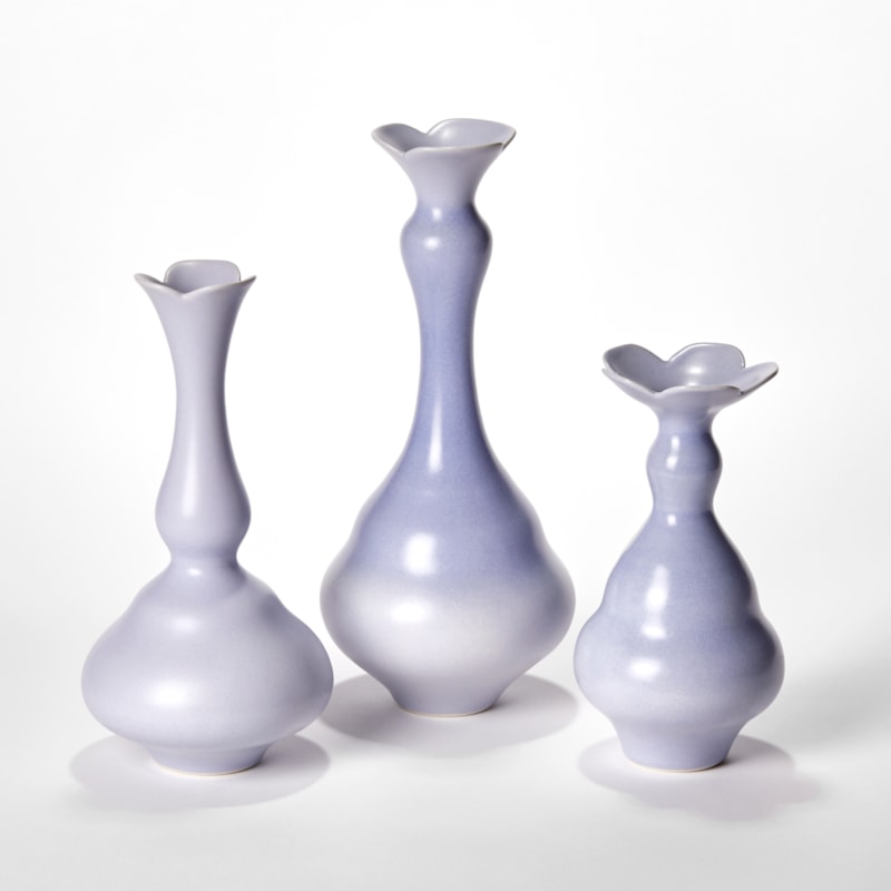 set of three porcelain vases in soft lilac purple each with wide rounded bases narrowing to long elegant necks each with abstract floral opening rims