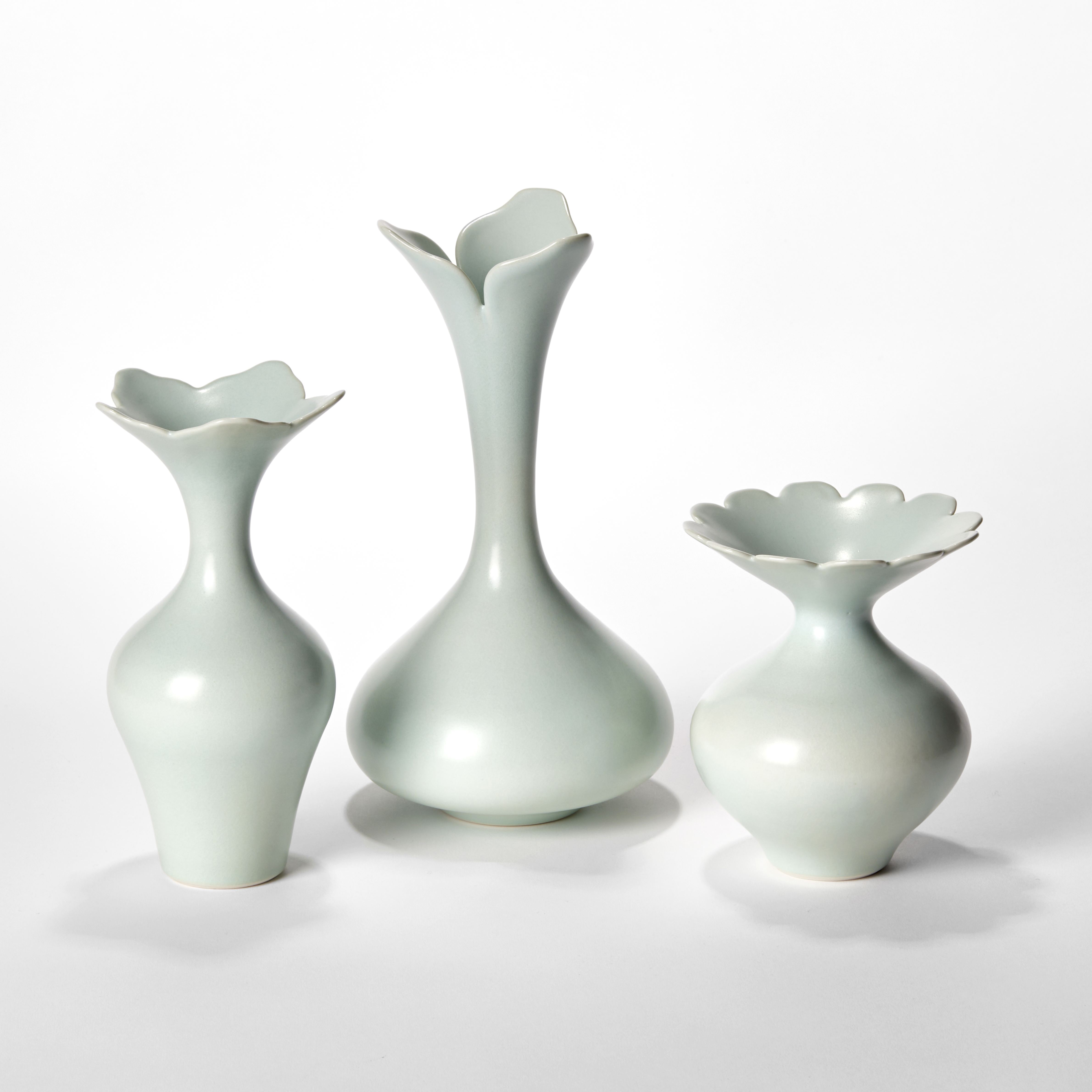 still life of three celadon coloured porcelain vases with rounded wide bases reaching to slender necks each with abstract flower opening rims