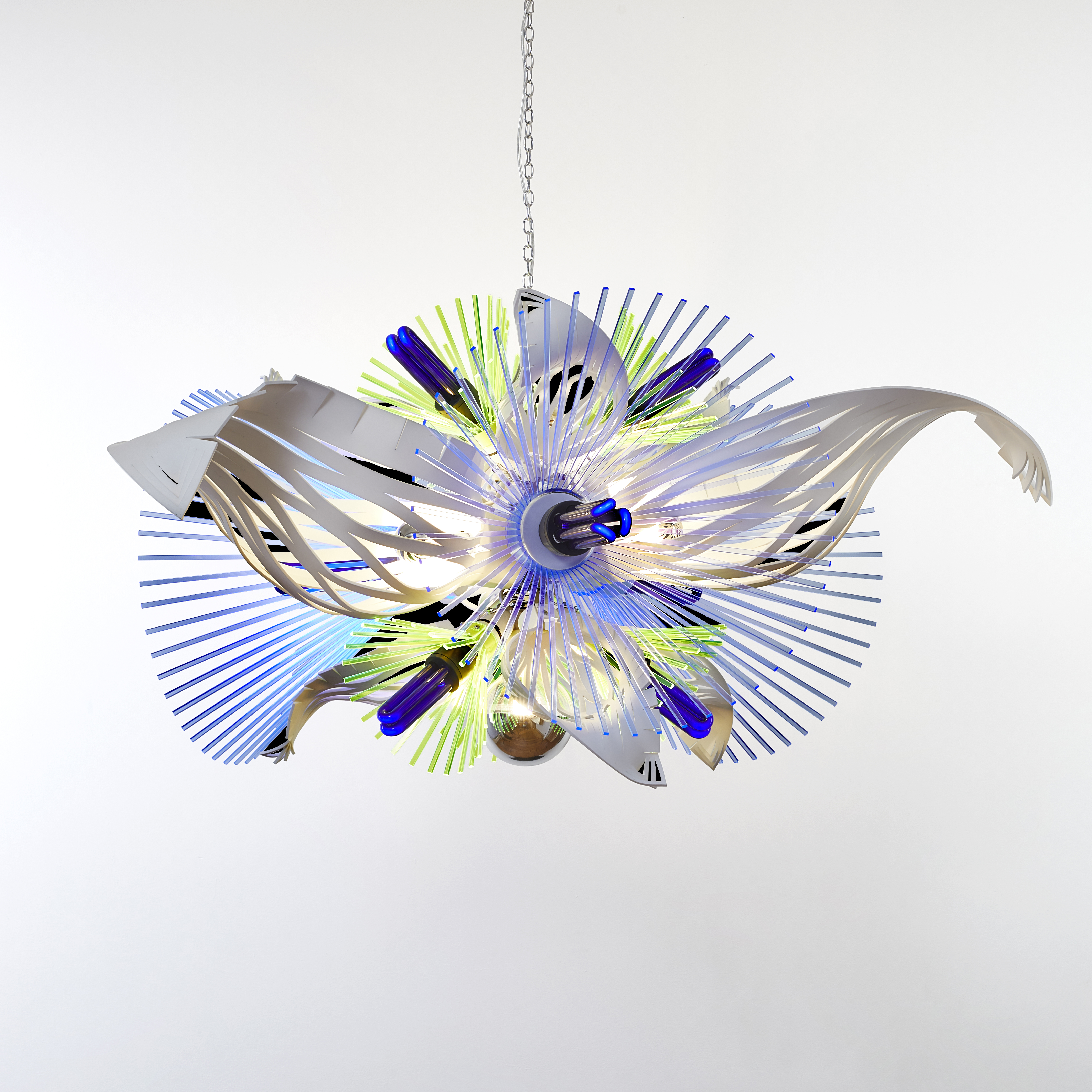 hanging sculptural light in white blue and green which resembles alien botany a vibrant mix of graphic repetitive organic three dimensional shapes with cutout sections and fronds made from acrylic with ultraviolet lightbulbs
