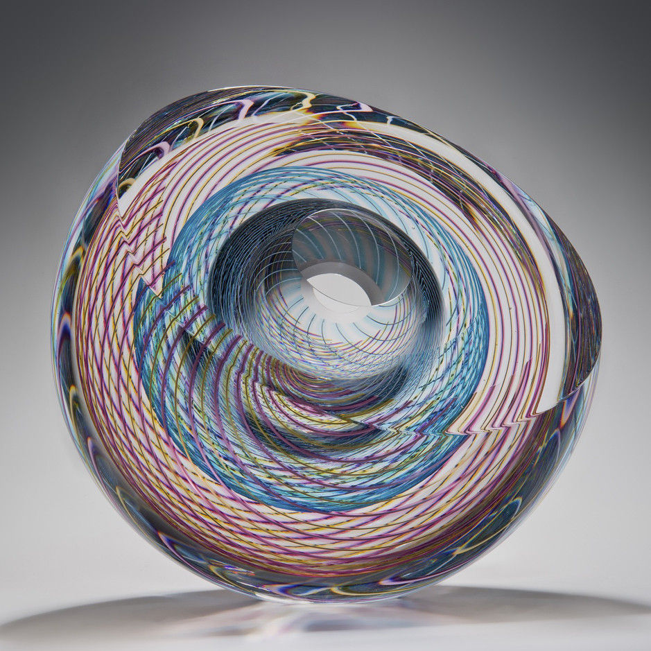 art glass sculpture in donut shape with geometric patterns in pink light blue and clear glass