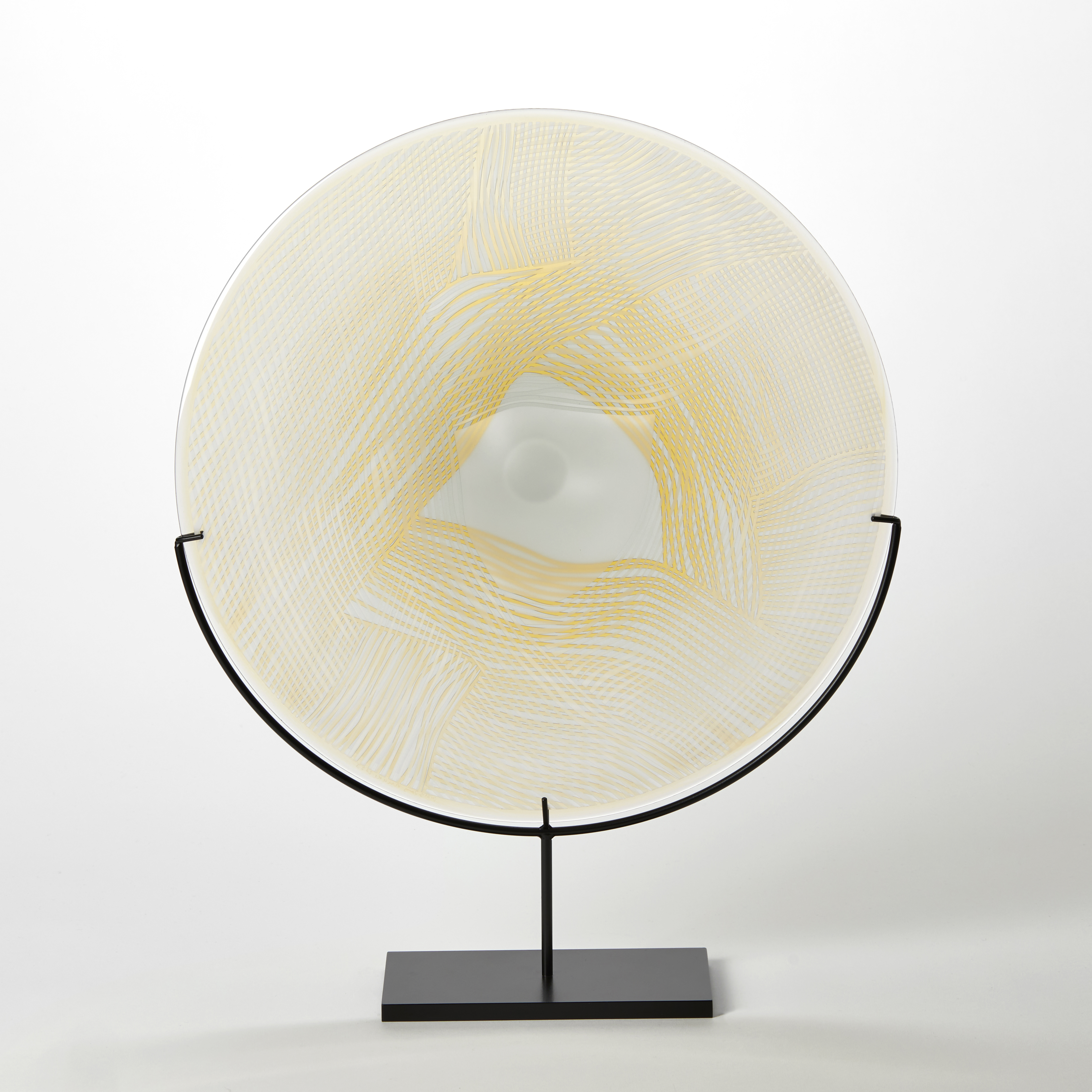 clear and soft amber gold and yellow glass plate with etched patterned surface presented on a black stand