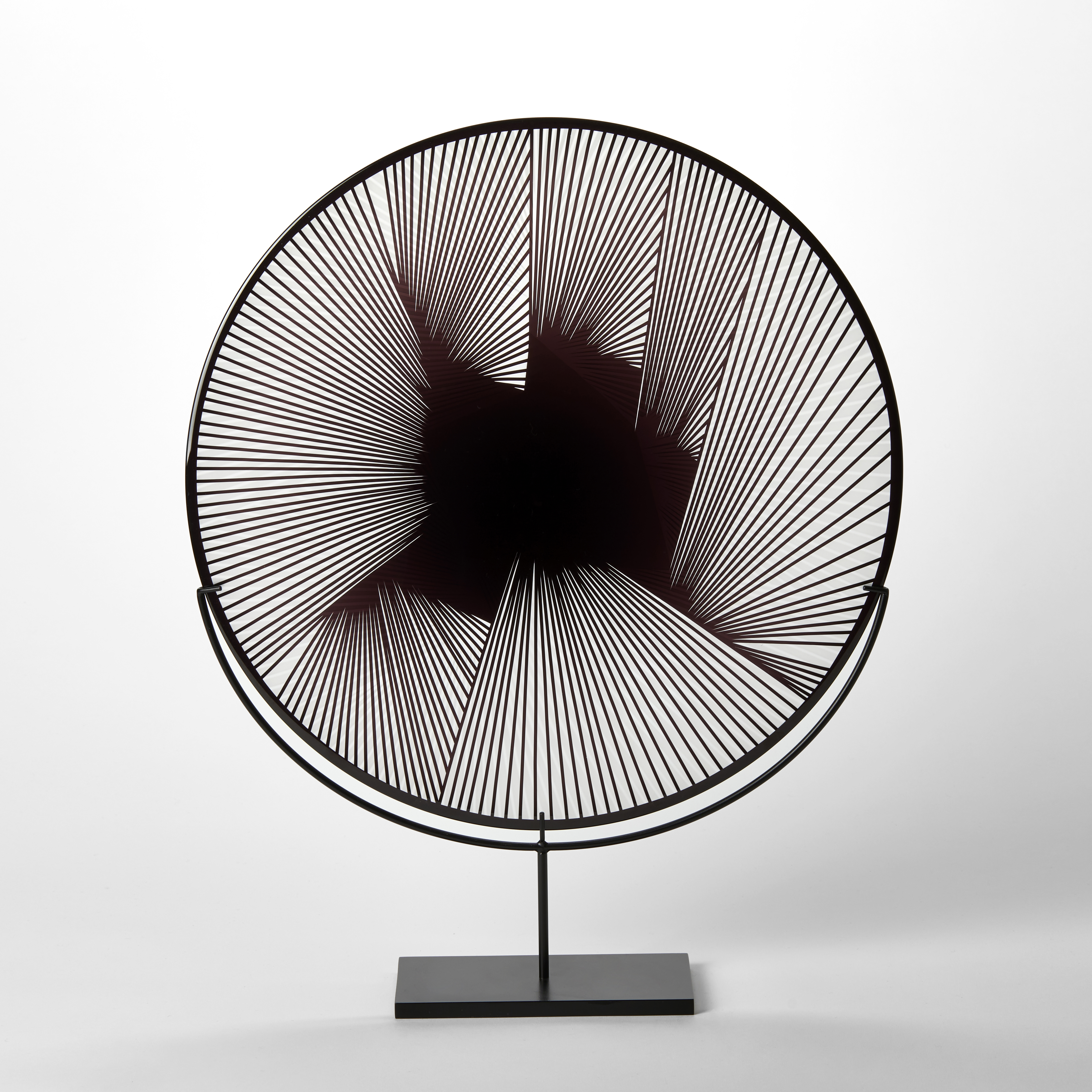 round clear and black hand blown glass decorative plate with abstract linear geometric etched lined pattern on the surface presented on a black steel stand