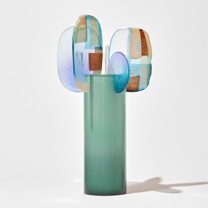 opaque soft celadon tall tube with five different shaped finials perched on the top edge spaced around the perimeter each with abstract patches of colour in lilac jade bronze and cream hand made from glass