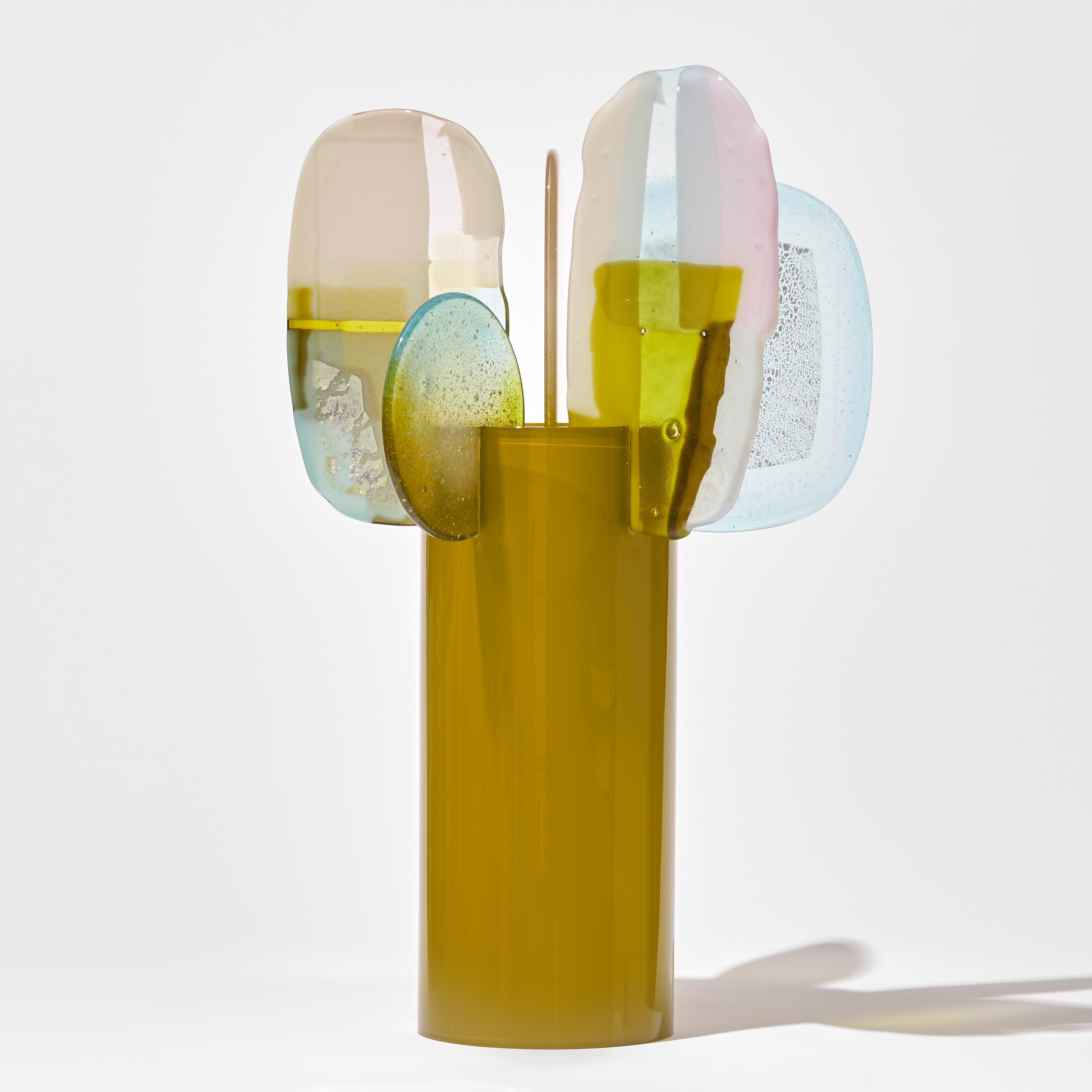tall glossy cylinder in mustard yellow with 5 flat finials perched standing upwards on the top edge in different soft rounded shapes with abstract surface patterns in aqua pink white and yellow hand made from blown and fused glass
