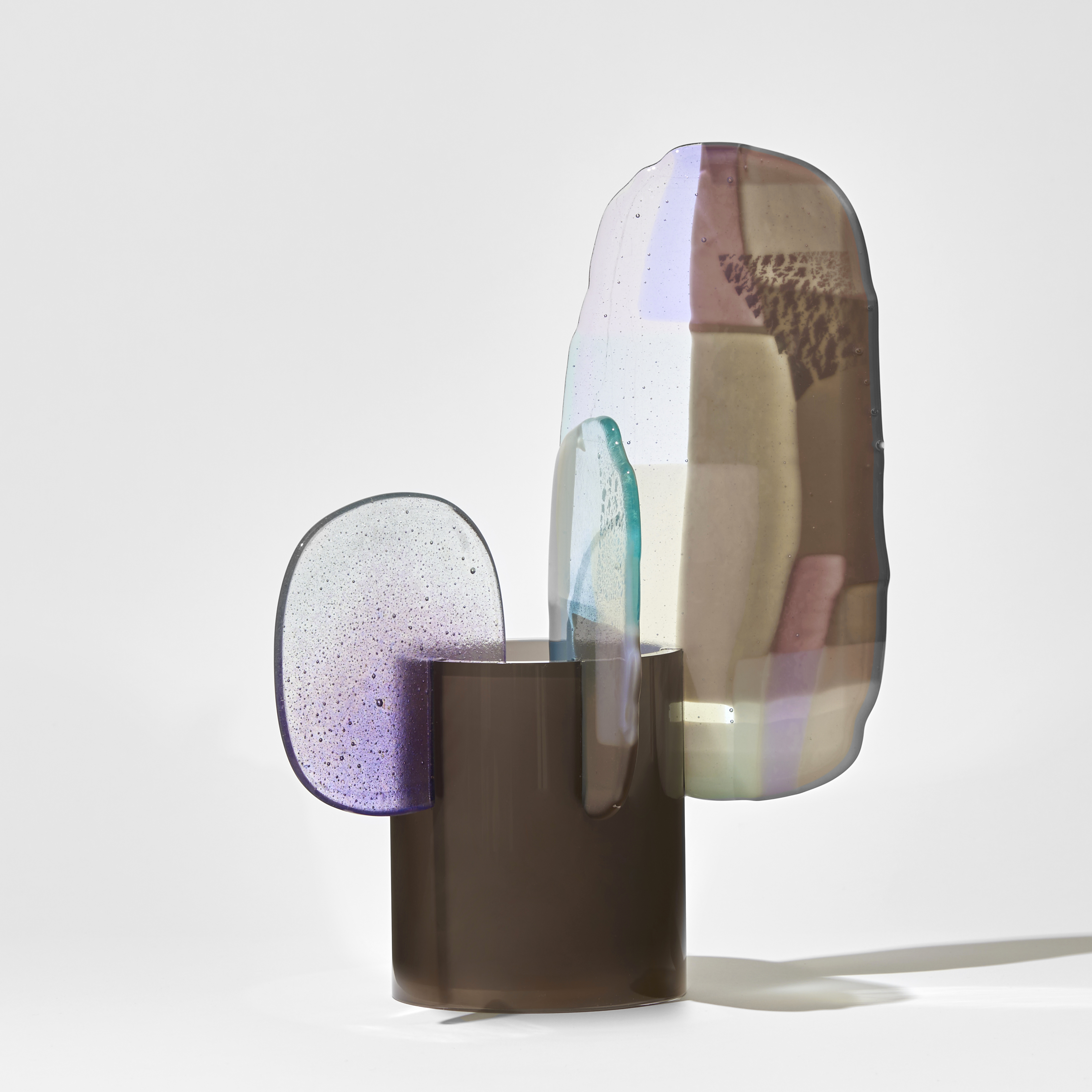 short opaque bronze brown cylinder with three different organic shaped finials perched on the rim with a mix of colours of pink lilac brown jade and cream hand made from glass