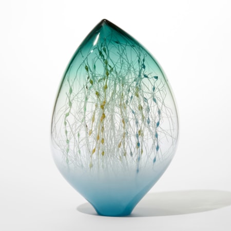 off centre glass ovoid sculpture with opaque light blue base transparent middle and sea green transparent top with the interior filled with a mass of fine straight and undulating canes in white ochre blue and teal