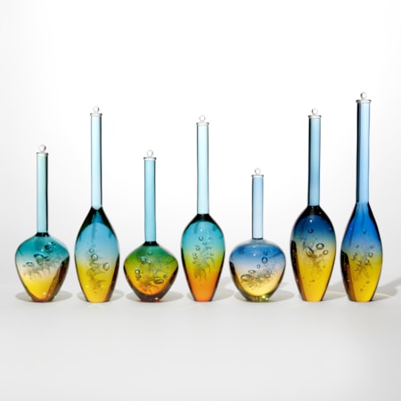 set of 7 different shaped solid transparent bottles with trapped bubbles inside each with a golden yellow bottom half merging to bright blue uppers all with long necks and stoppers on the top