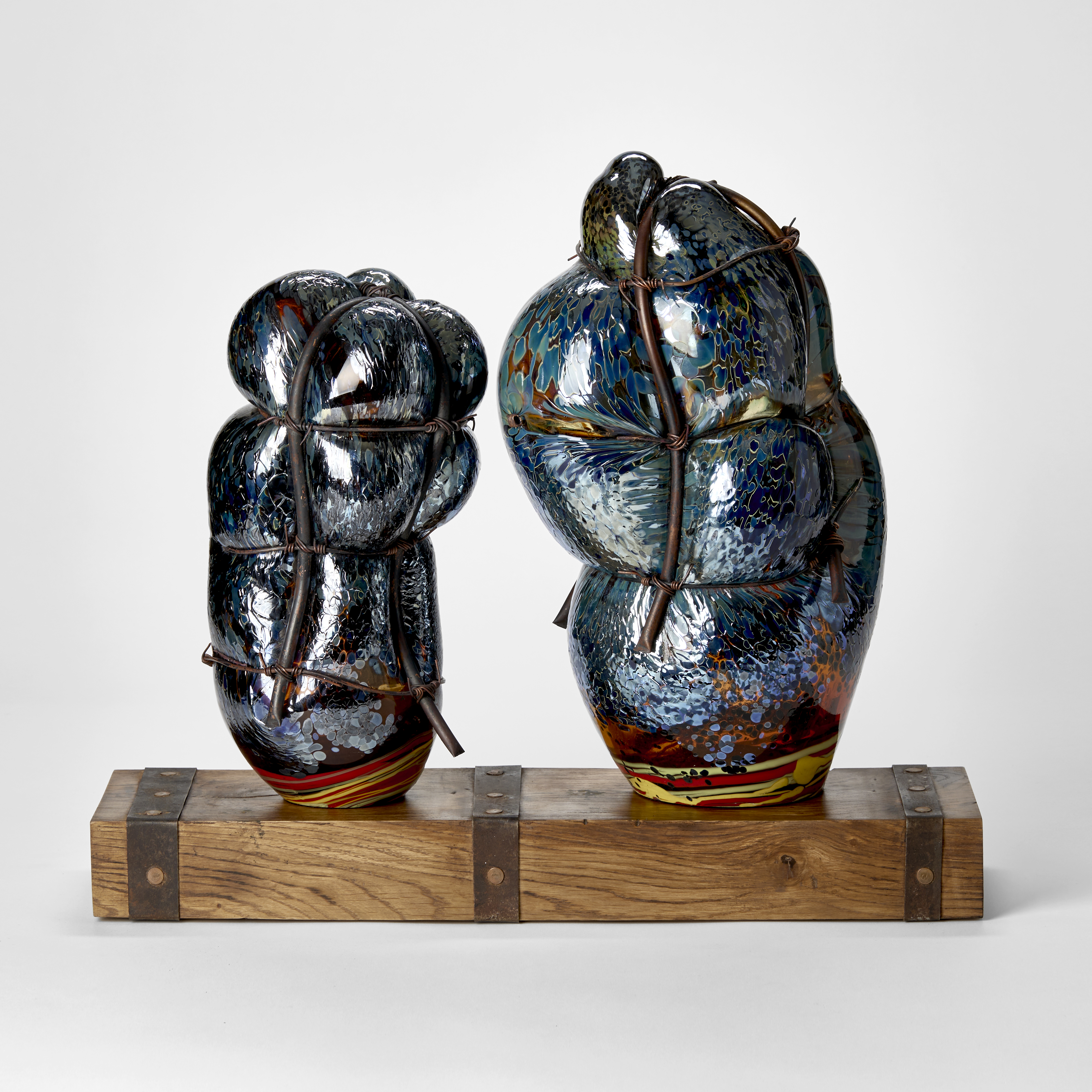 wooden rustic base with ages metal straps dividing the surface into two areas with two abstract simplified figures standing on the top hand made from glass and each bound in copper pipe representing a mother and child