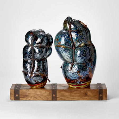 wooden rustic base with ages metal straps dividing the surface into two areas with two abstract simplified figures standing on the top hand made from glass and each bound in copper pipe representing a mother and child