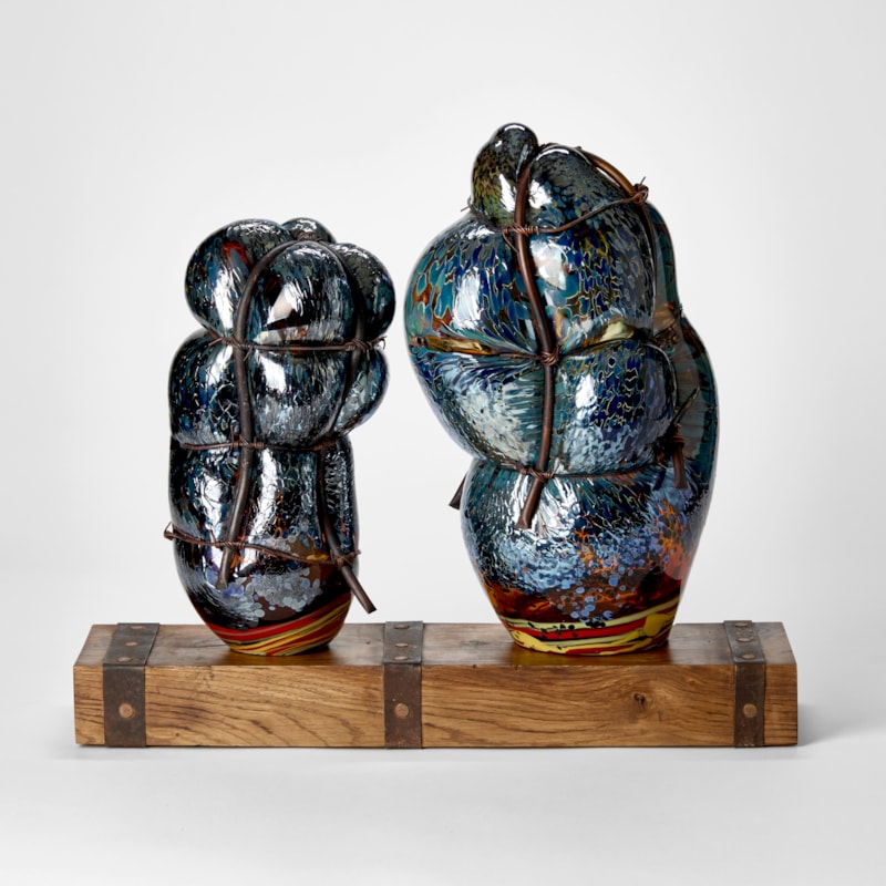 wooden rustic base with ages metal straps dividing the surface into two areas with two abstract simplified figures standing on the top hand made from glass and each bound in copper pipe representing a mother and child