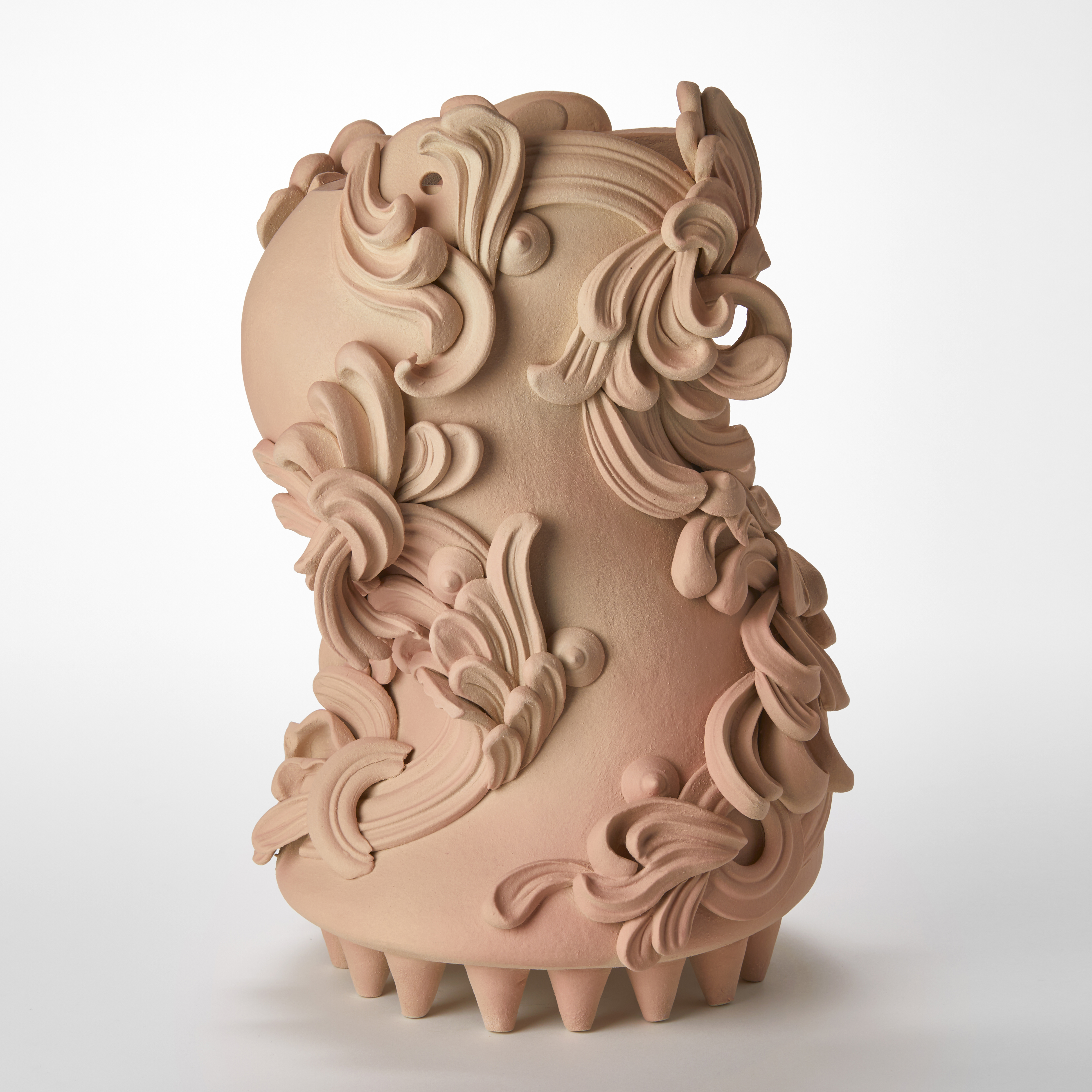 bloated s shaped sculptural vessel in dusty peach pink and beige held aloft on a multitude of small cone shaped feet on the base covered in architectural swirls and curls hand made from white st thomas clay