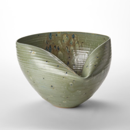 round hand thrown bowl with one folded in side creating a neat inward tuck with slight horizontal ridges on the surface in a soft sage green colour with dark blue smudgy dots hand thrown from white saint thomas clay