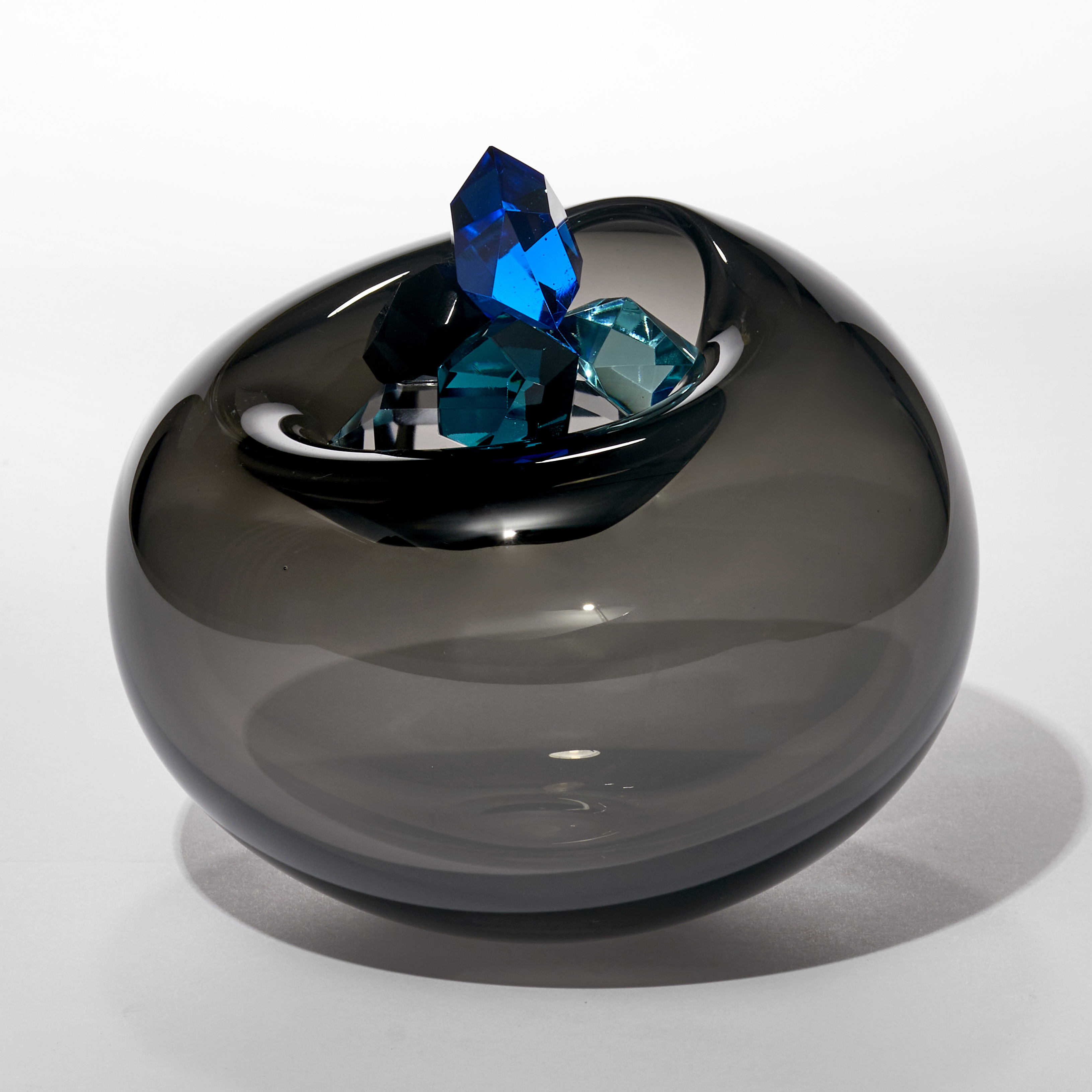 transparent dark grey round bubble with soft top opening cradling a stacked cluster of vibrantly coloured cut gems in blue jade turquoise emerald and amber hand made from blown and cut glass