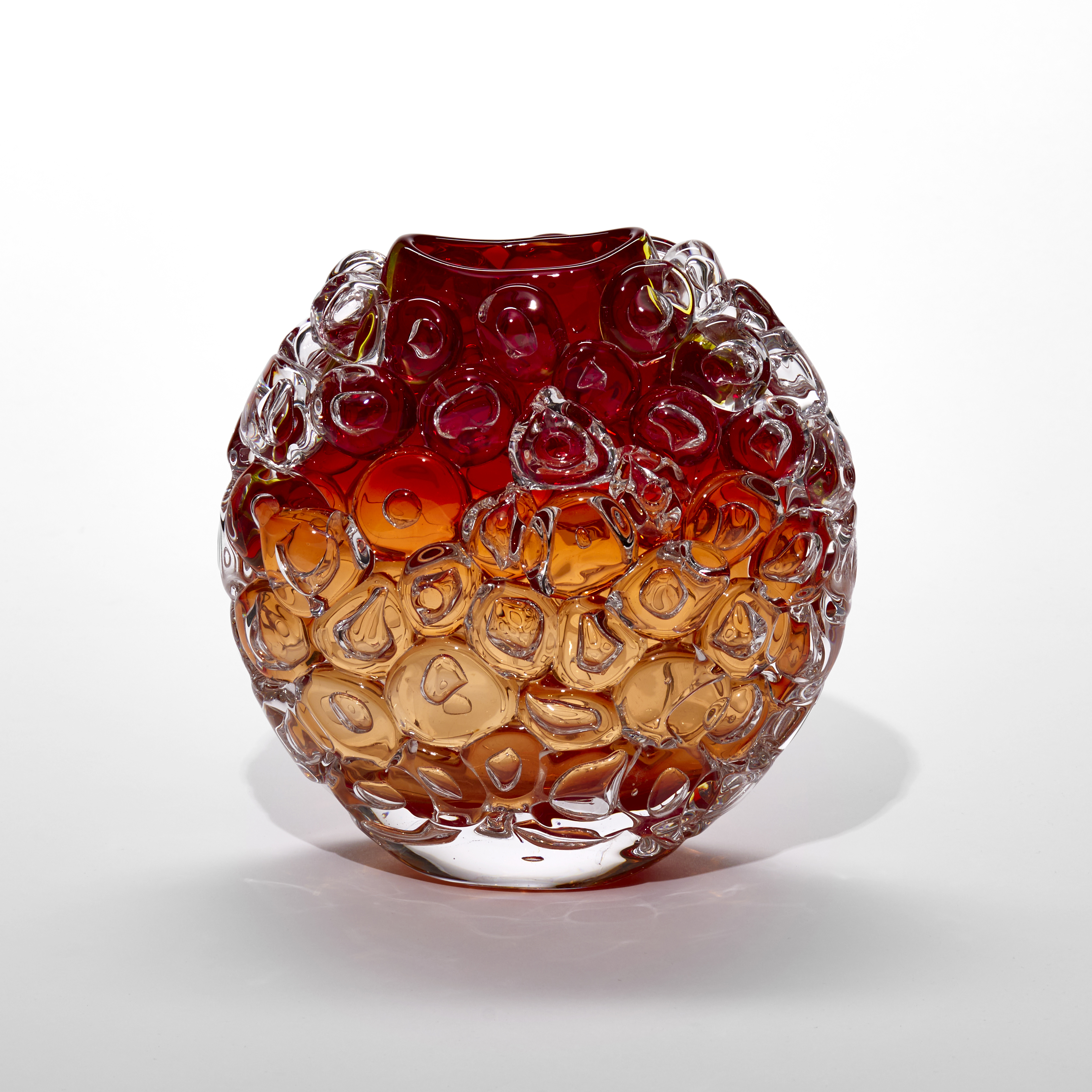 rounded transparent vase with flat front and back covered in large oversized bubbles like bubblewrap fading from light amber orange at the base through to dark oxblood red at the top with an elegant curved top opening hand made from blown glass