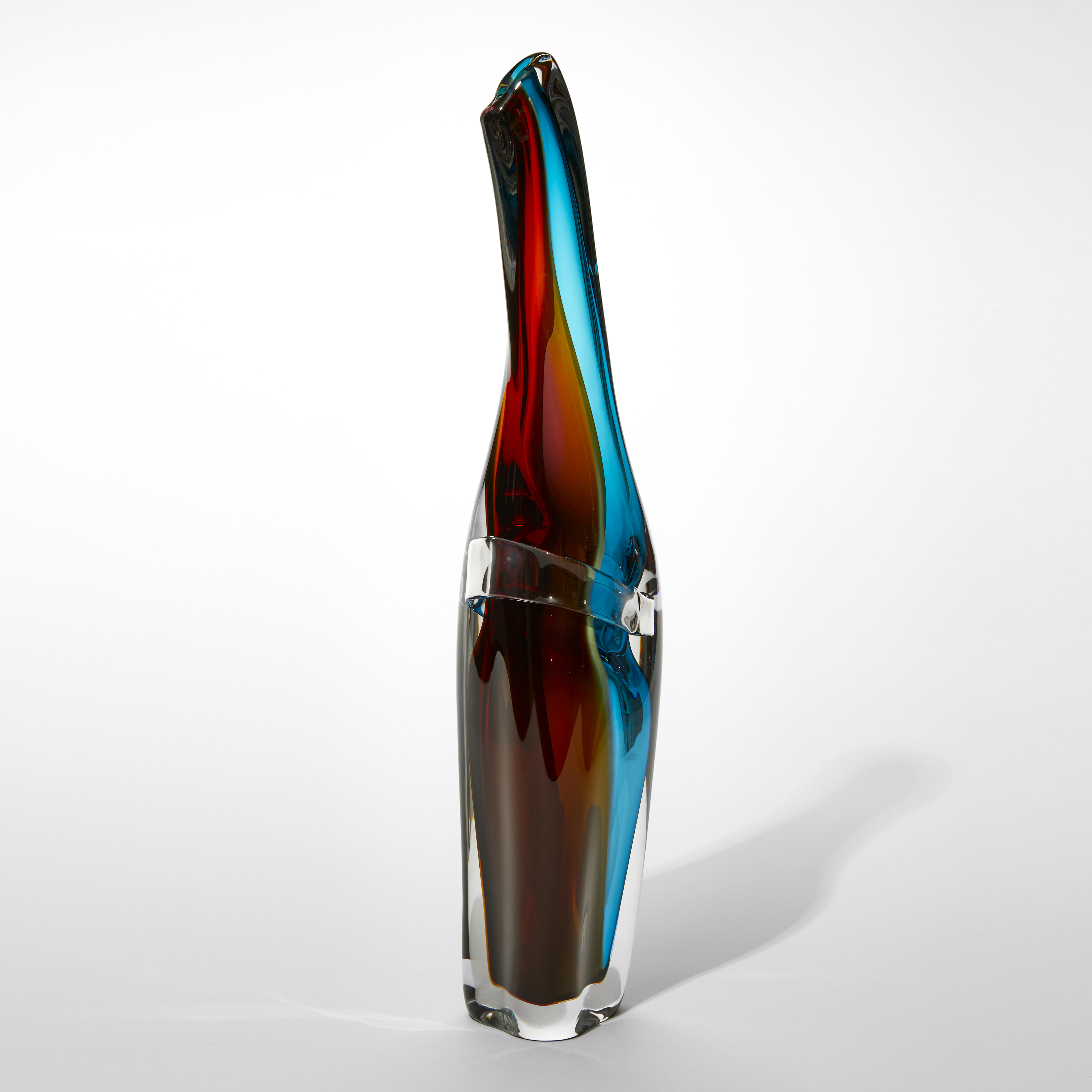 tall soft tapering sculptural vase with bands of transparent colour in red burnt orange and dark turquoise with an outer layer in clear hand made from blown glass