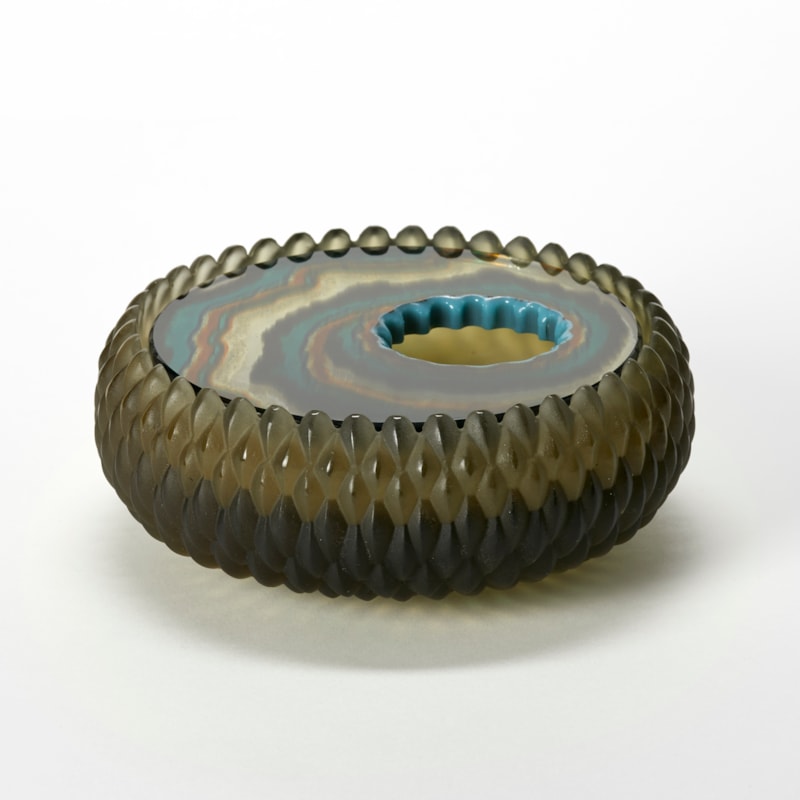 round low box with curved sides and an opaque matt exterior surface with a relief repeat diamond pattern in bronze olive green and an inset polished lid with organic bands of colour in rust black jade green and brown hand made from glass
