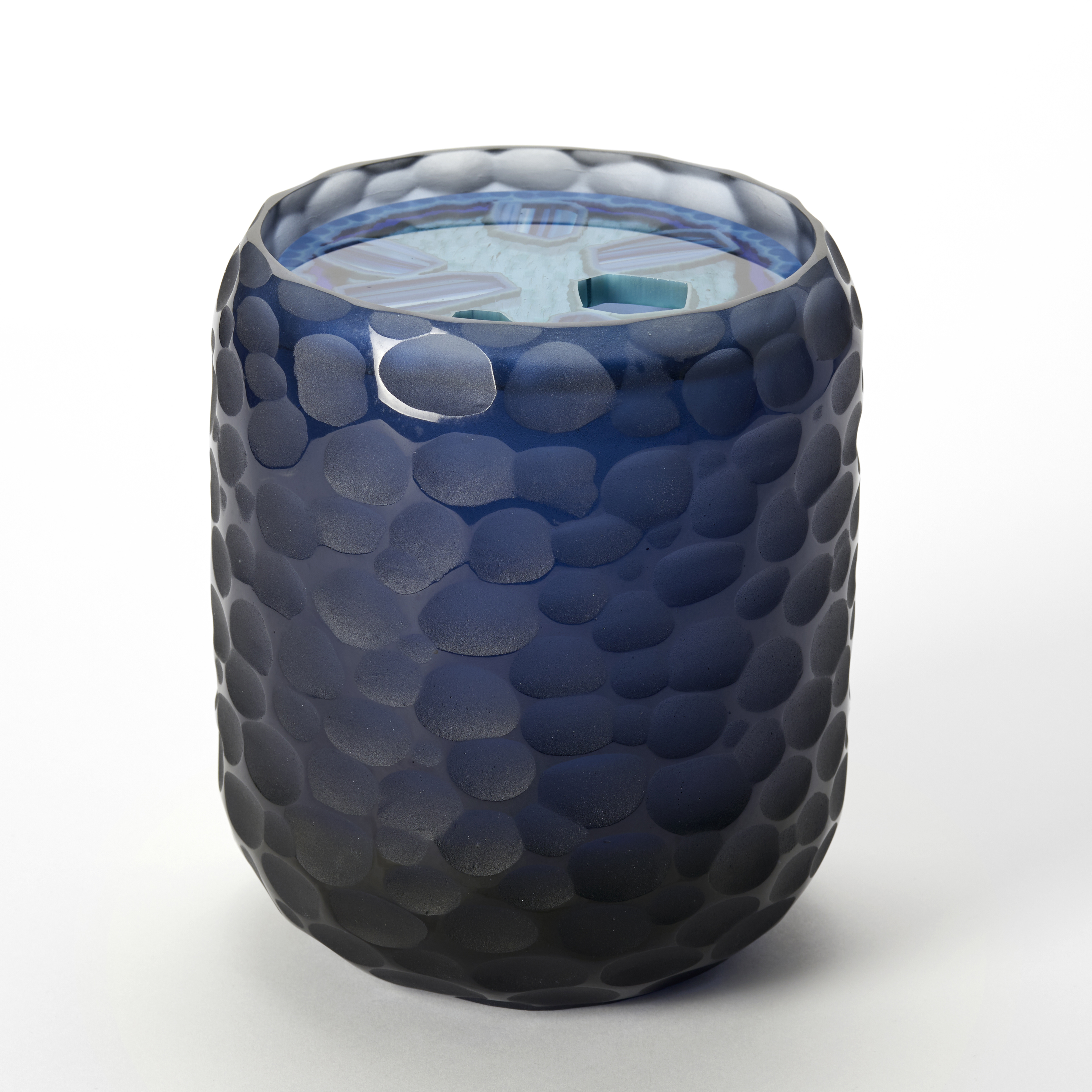 stumpy tubular opaque vessel in dark midnight blue with organic randomly scalloped outer surface and top round opening with an inset disc shaped lid with a polished surface and stylised agate pattern trapped within in blue jade and turquoise handmade from glass 