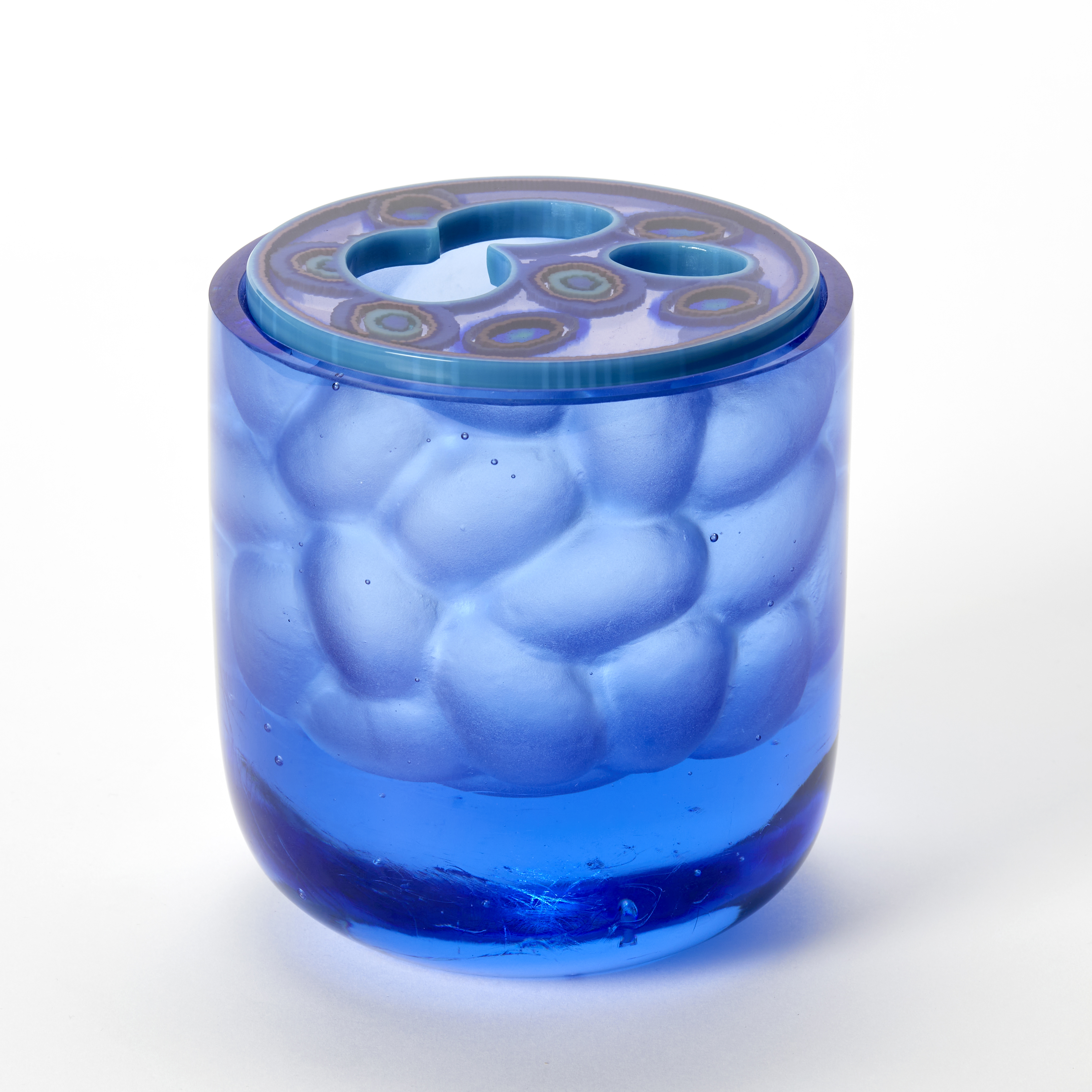 intense rich transparent blue short tubular vessel with smooth exterior and rounded base with a repeat bumped carved interior walls with a round top opening and patterned flat lid with amoeba organic patterned details captured within hand made from cast glass