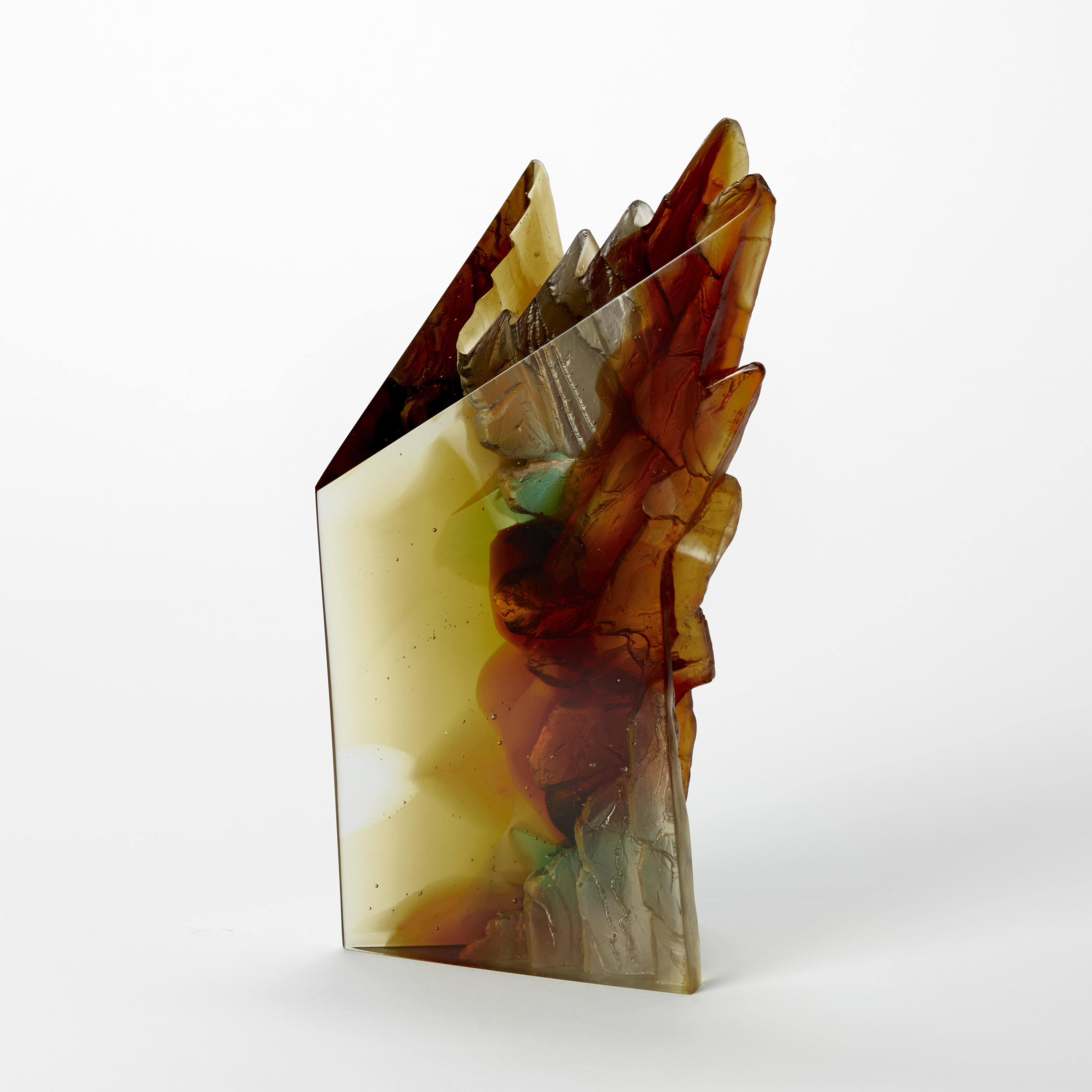 solid standing sculpture with two flat glossy sides and two inverted sides with a craggy cliff like texture hand made and cast from transparent amber green and burnt orange coloured glass