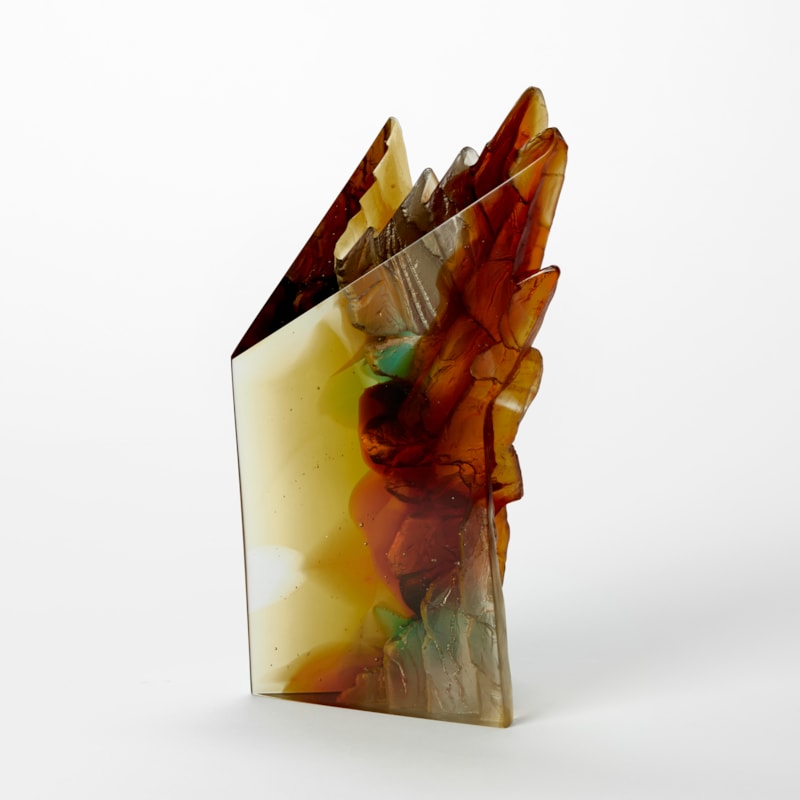 solid standing sculpture with two flat glossy sides and two inverted sides with a craggy cliff like texture hand made and cast from transparent amber green and burnt orange coloured glass