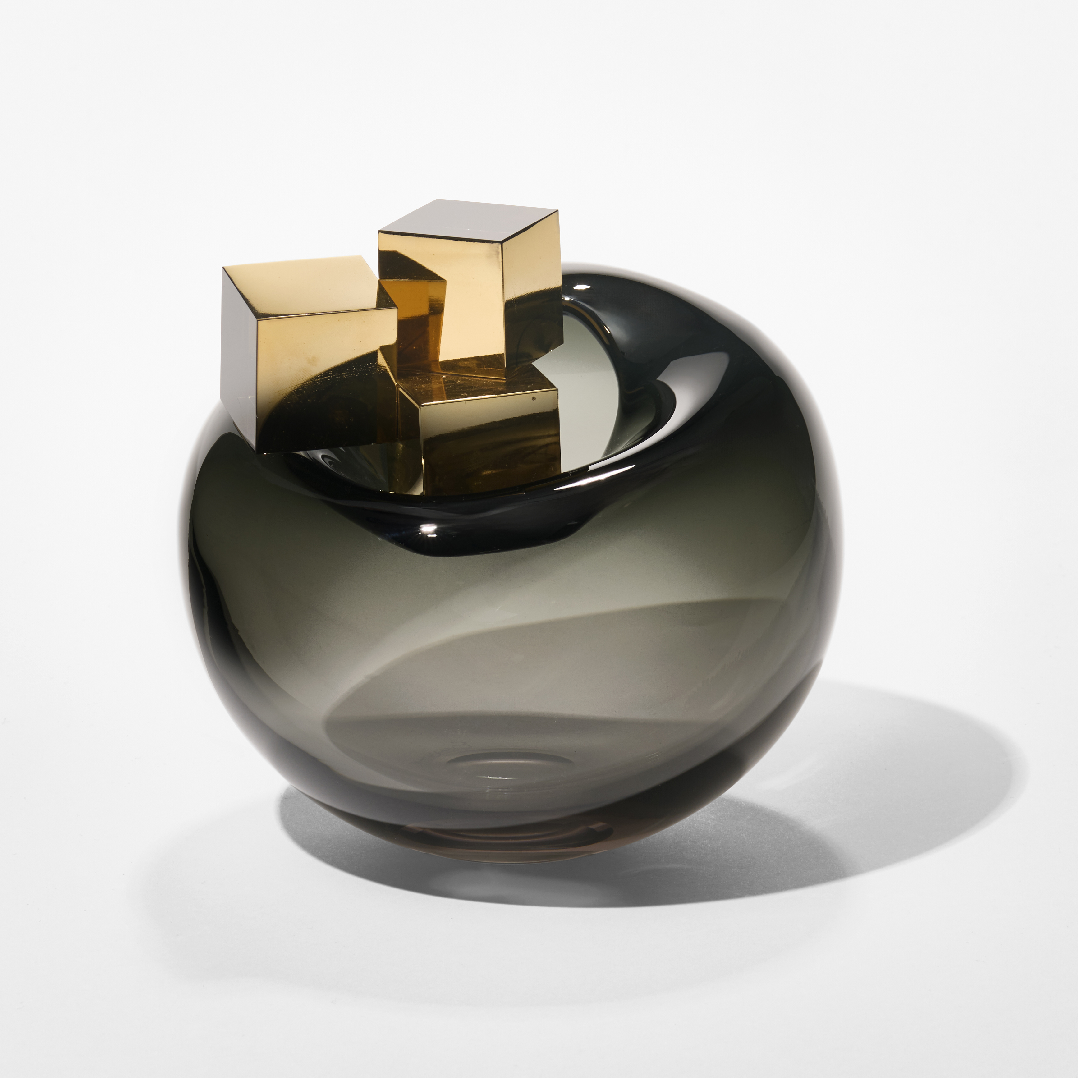 a smokey dark grey transparent round bubble with three different sized gold cubes perched on the top place by a small rounded opening hand blown from glass with gold lustre