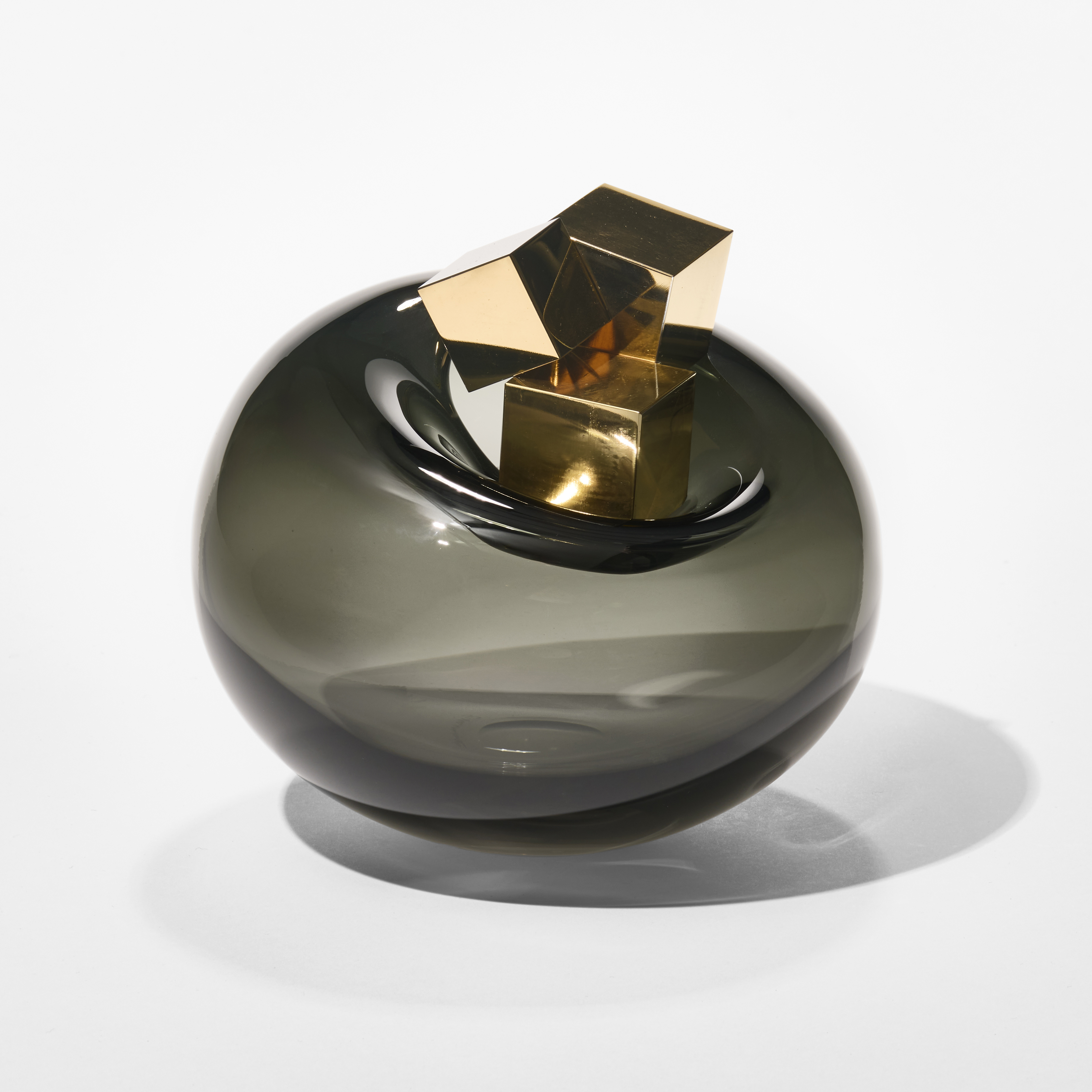 dark grey transparent round bubble with a small round opening at the top with three different sized gold cubes balanced beside it hand made from glass and gold lustre