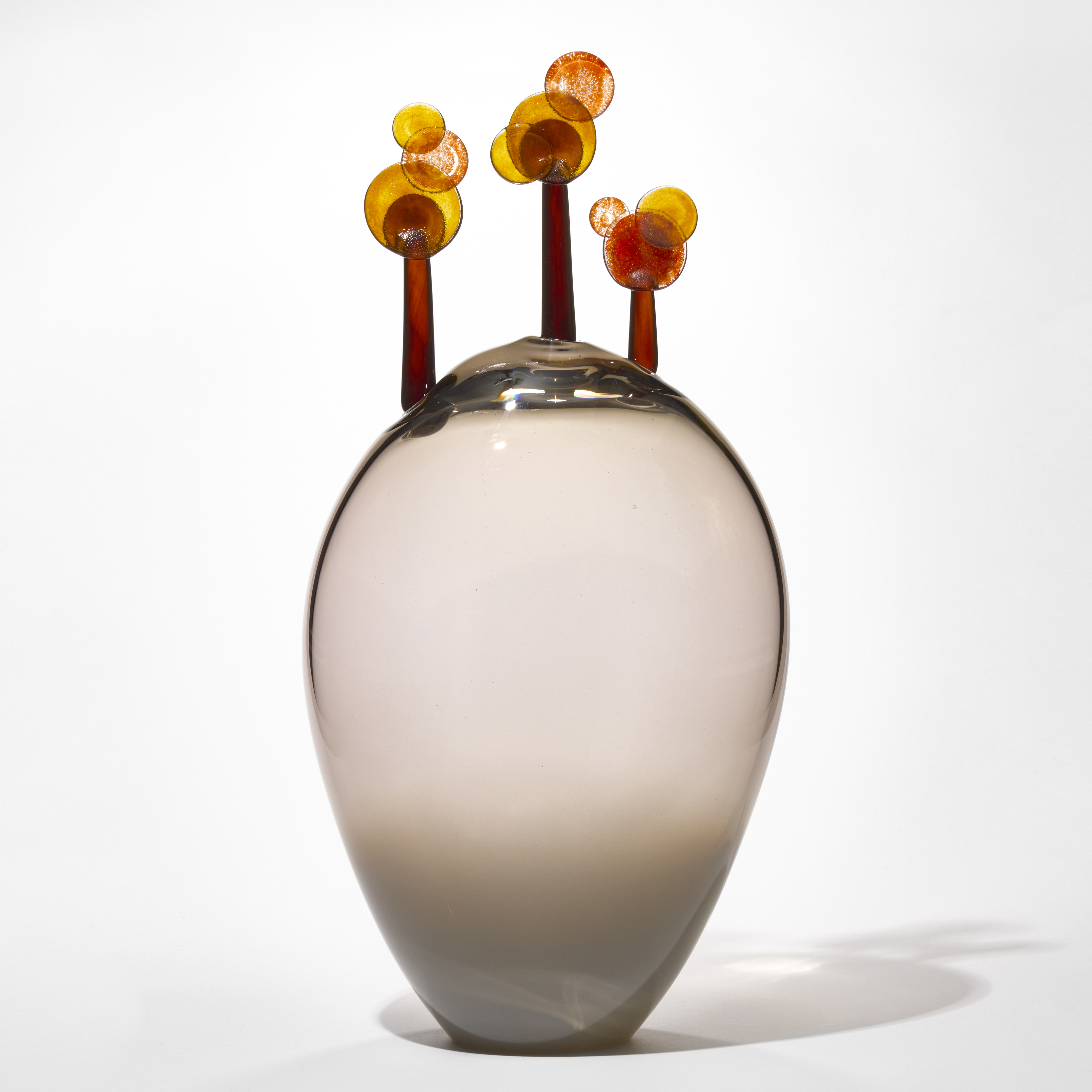 tall transparent soft mid grey oval shaped form with three small trees perched on the top each with red umber trunks and round lollipop leaves in amber and gold hand blown from glass