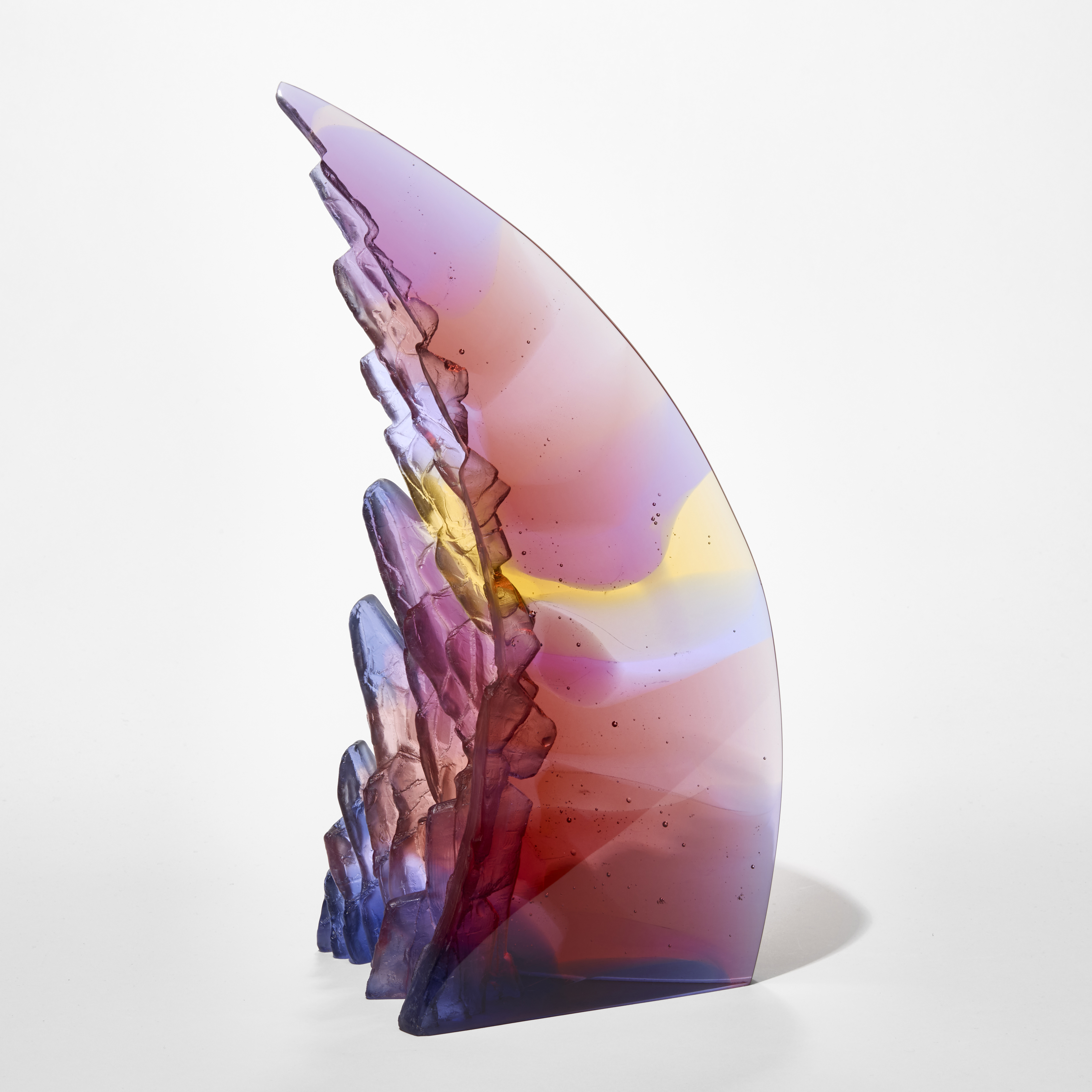 curved and leaning standing transparent pyramid with two glossy sides and one covered in rock like textures with areas in pink purple yellow and light blue hand made from cast glass