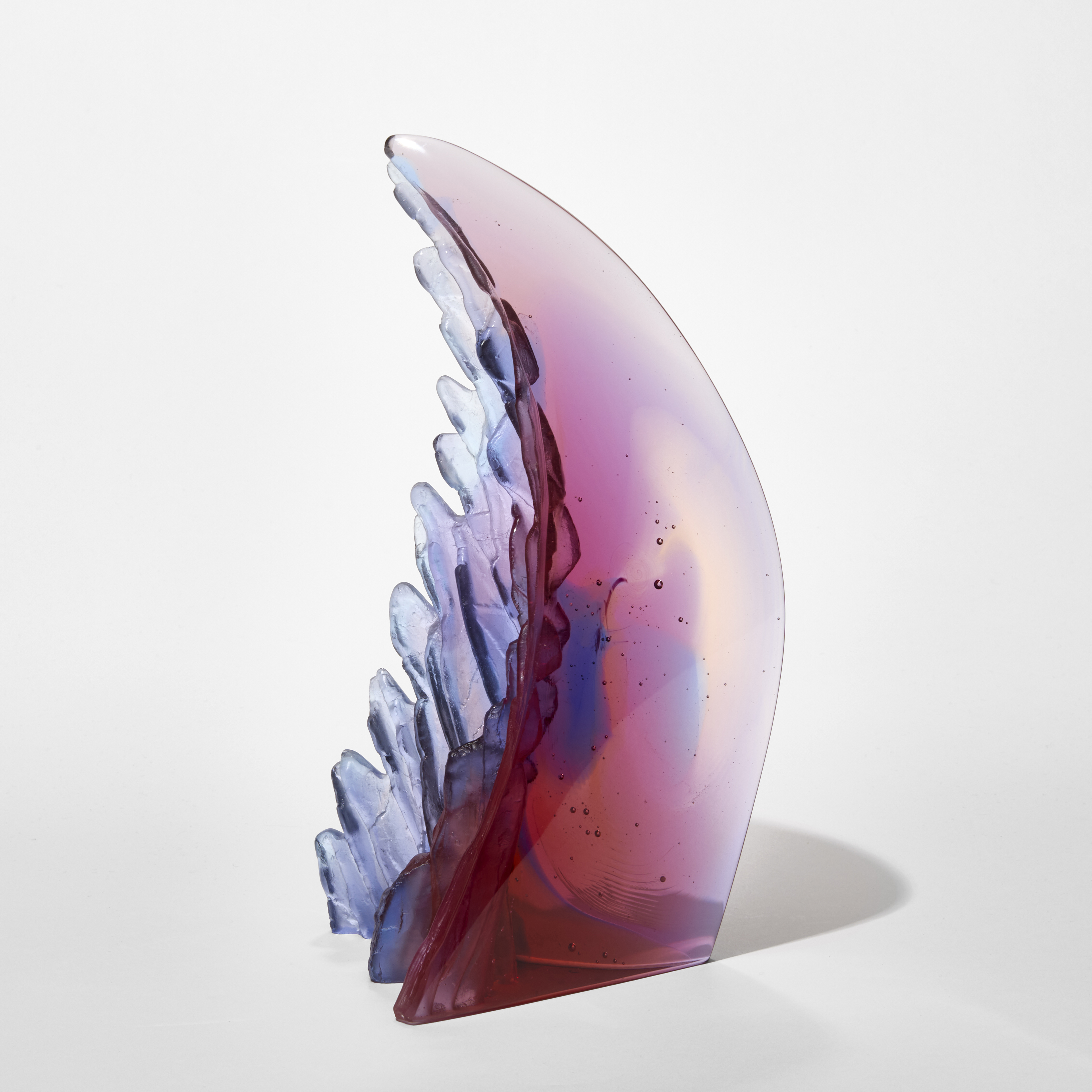 curved transparent claw like sculpture with two glossy sides and one jagged with rock like texture in merged pink blue purple and peach hand made from cast glass