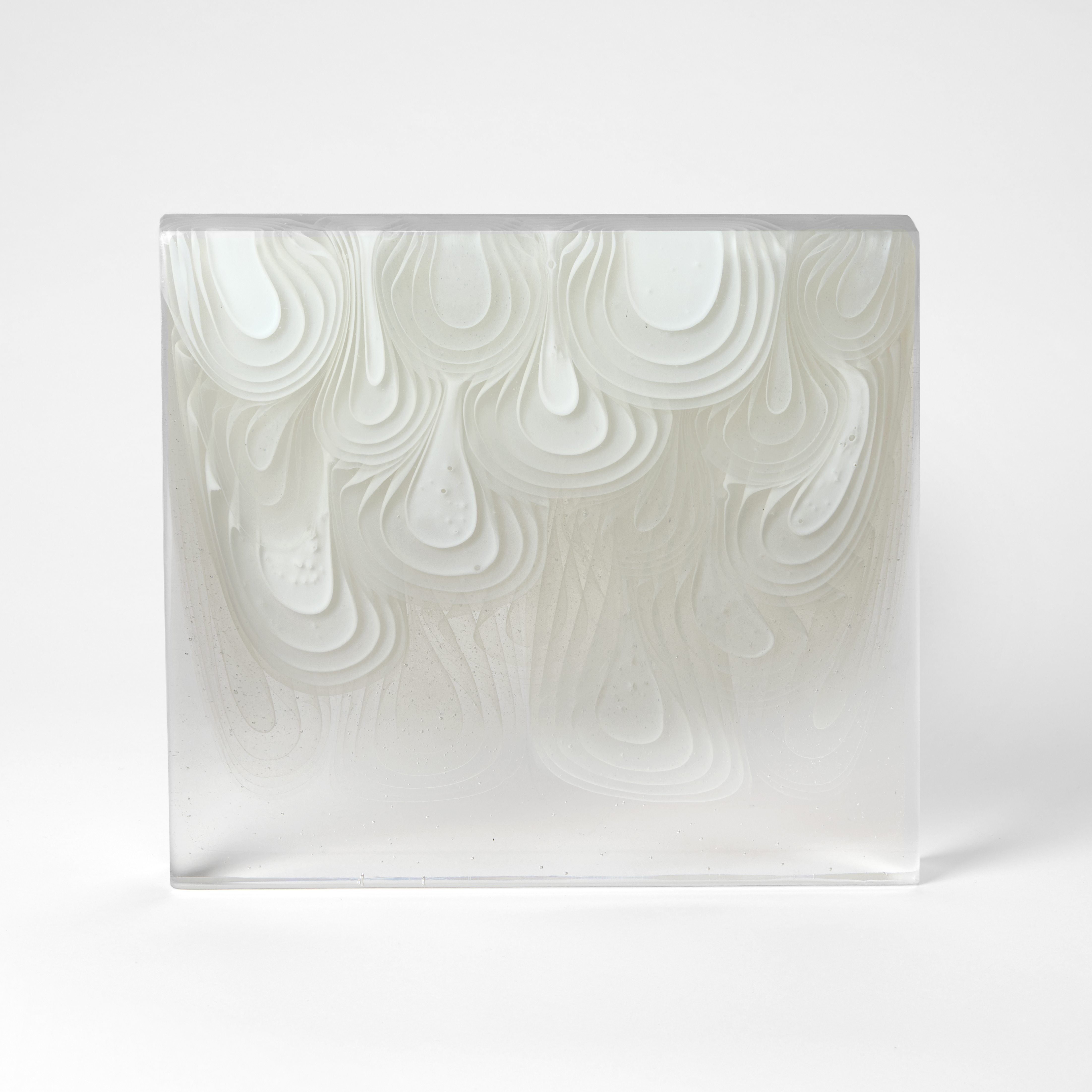standing rectangular clear block with concentric droplets in opaque white flowing from the top edge down through the form hand made from cast glass