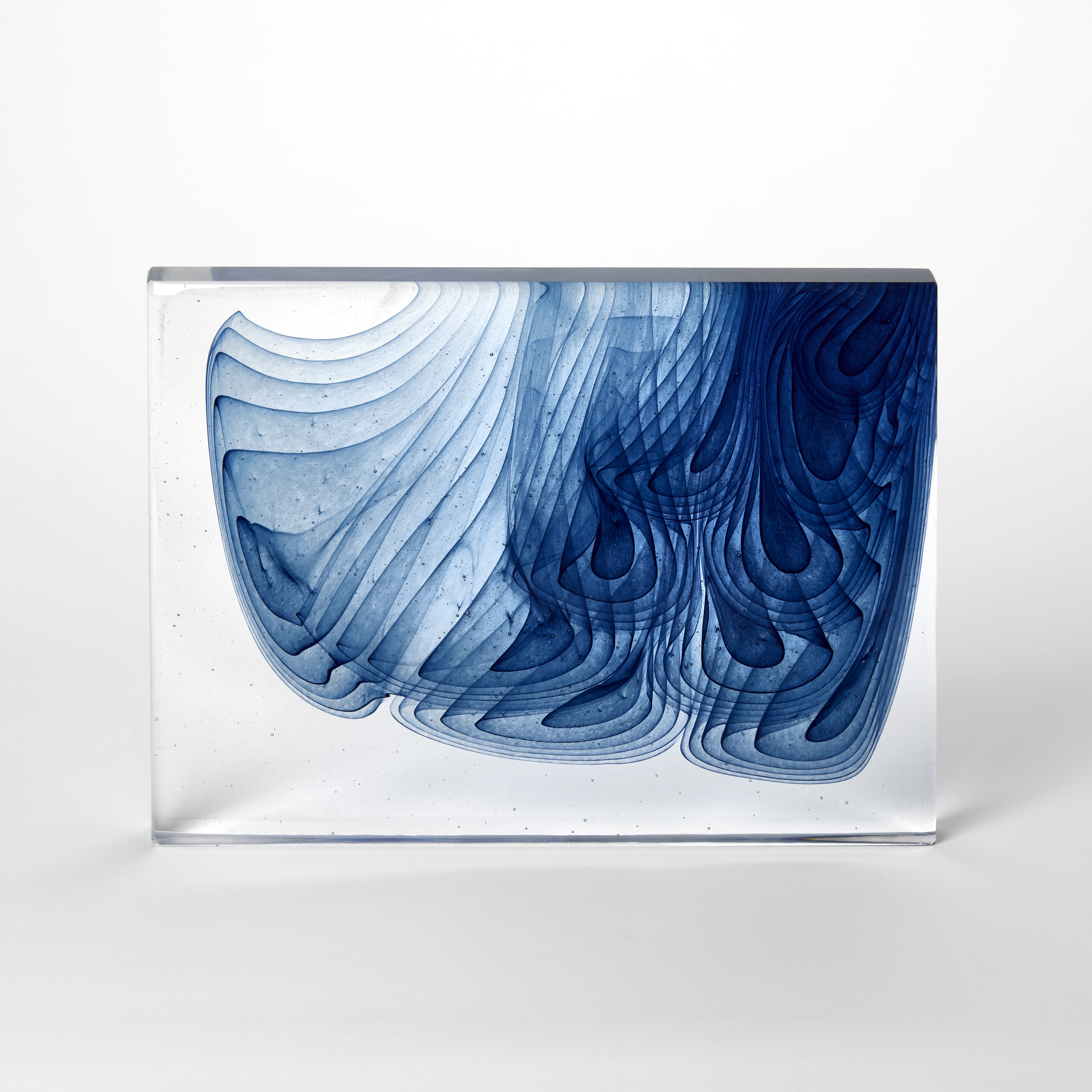landscape standing clear rectangular slab with a mass of concentric clustered blue droplets emerging from the top right hand corner spreading downwards across the form hand made from cast glass