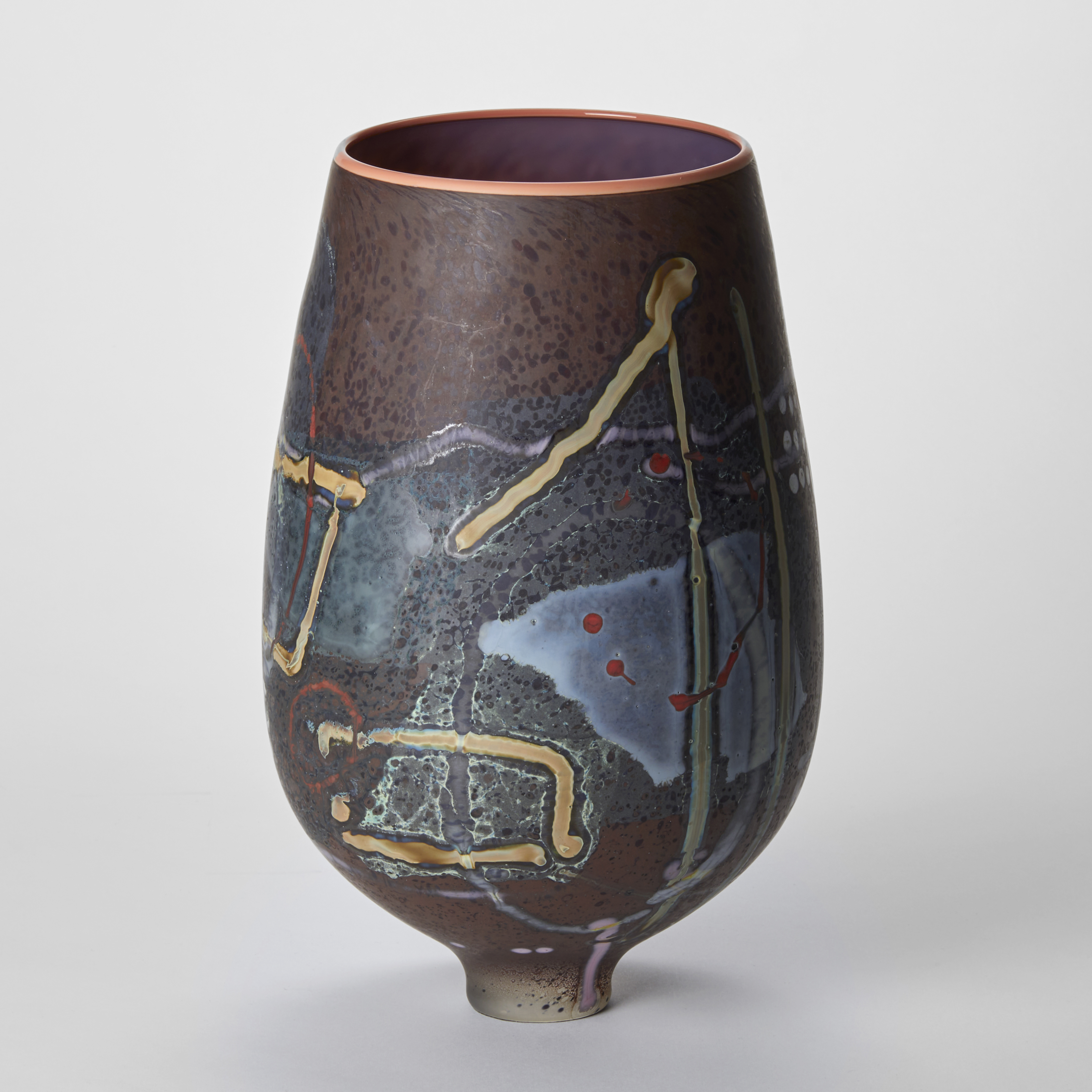 tulip flower shaped vase with a rich aubergine  glossy interior salmon pink rim and a matt exterior covered in abstract patterns and lines in blue lilac chocolate red and olive hand made from glass perched on an elegant tapering foot