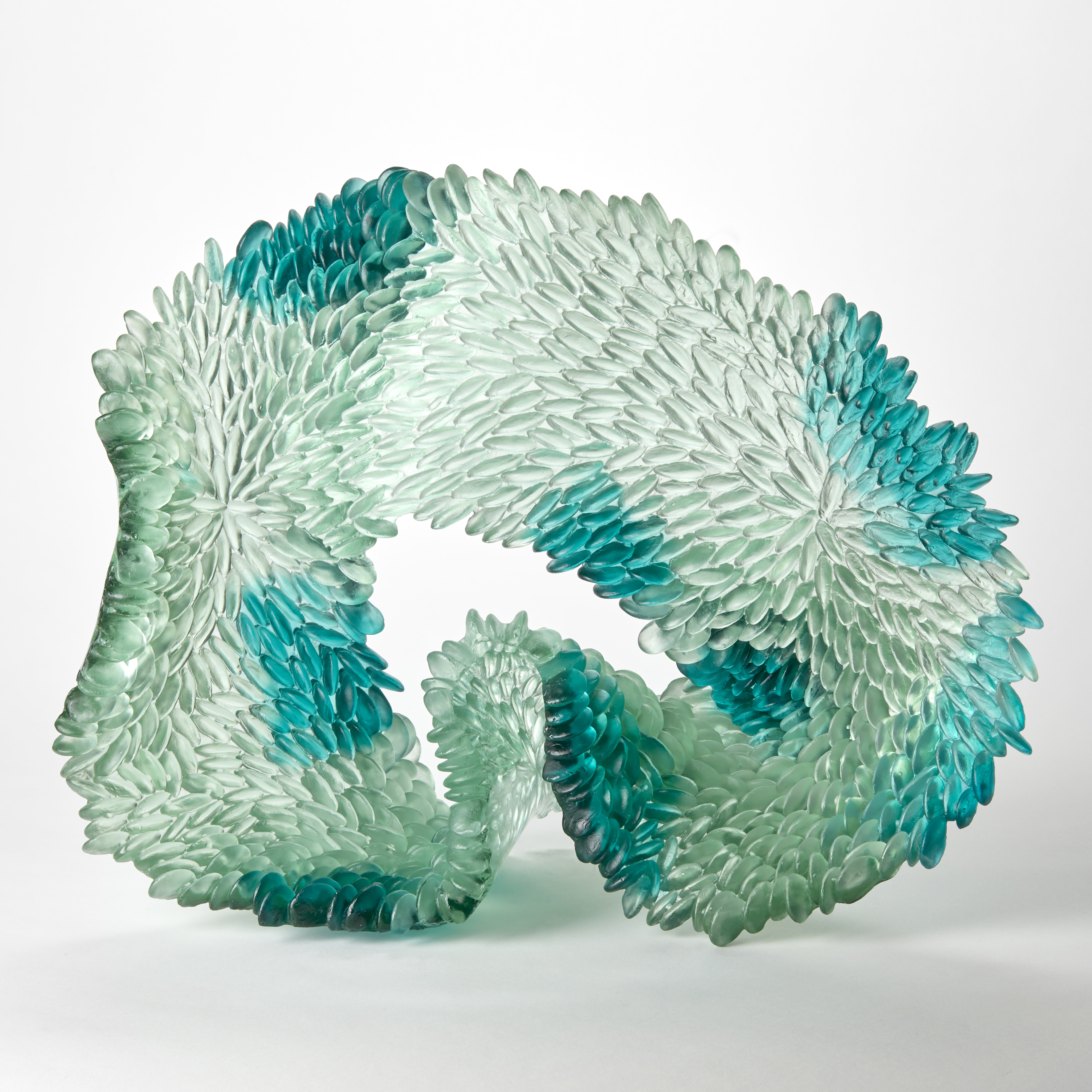 standing opaque ringed oval form with humped base section and front face covered in raised scales in jade celadon aqua clear and green handmade from cast glass