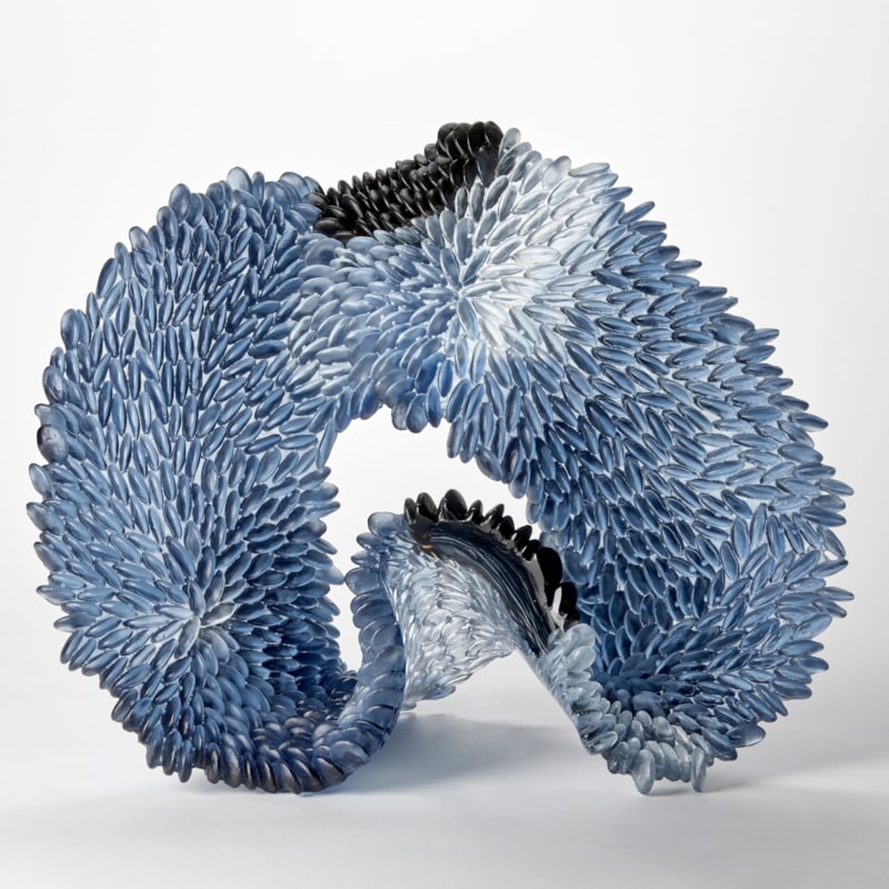 blue clear and black opaque standing looping wide banded organic sculpture with front face covered in raised scales hand made from cast glass