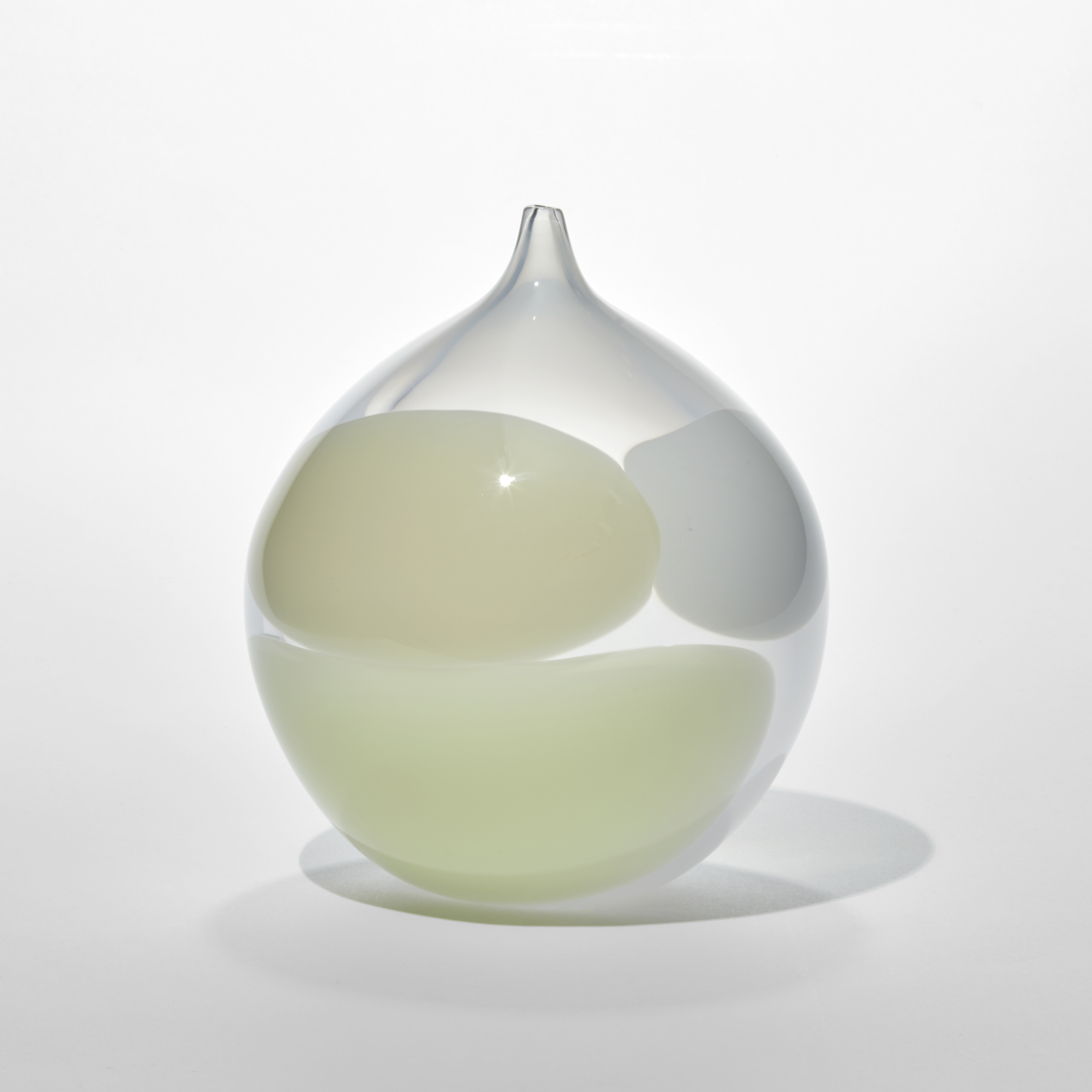 hand blown round dew drop shaped vessel with small pointed opening made from milky semi transparent glass with three rounded blobs on the surface in opaque white cream and yellow