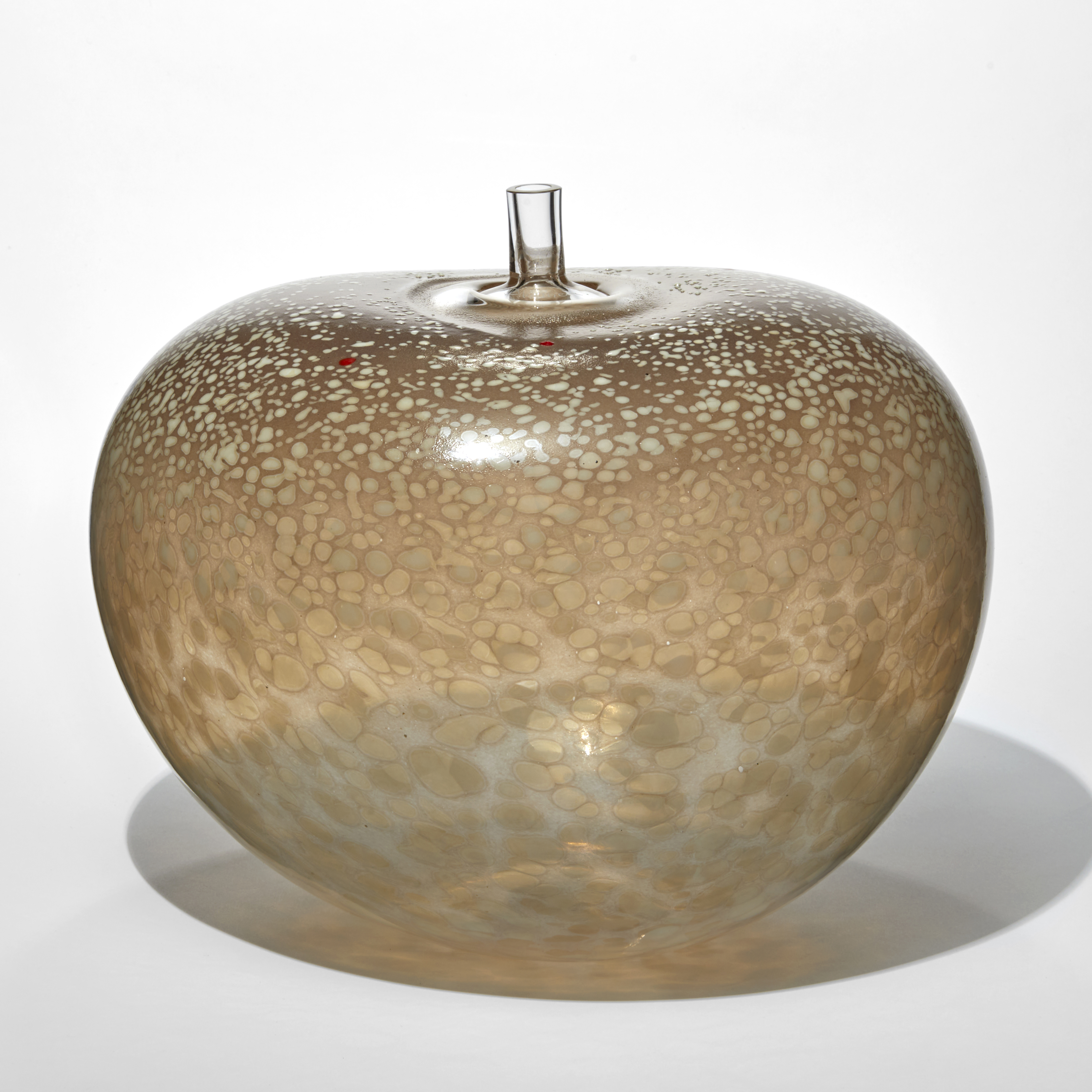 rounded bean shape vessel in transparent taupe with a mottled and spotted surface in beige and cream with a clear short tubular stem sticking out from the top hand made from glass