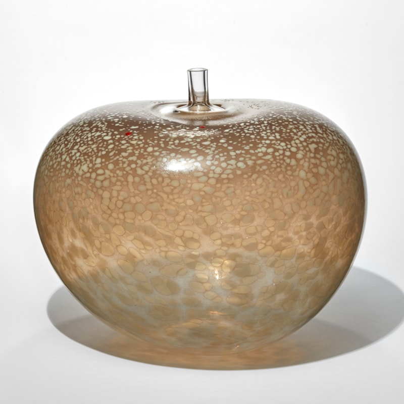 rounded bean shape vessel in transparent taupe with a mottled and spotted surface in beige and cream with a clear short tubular stem sticking out from the top hand made from glass