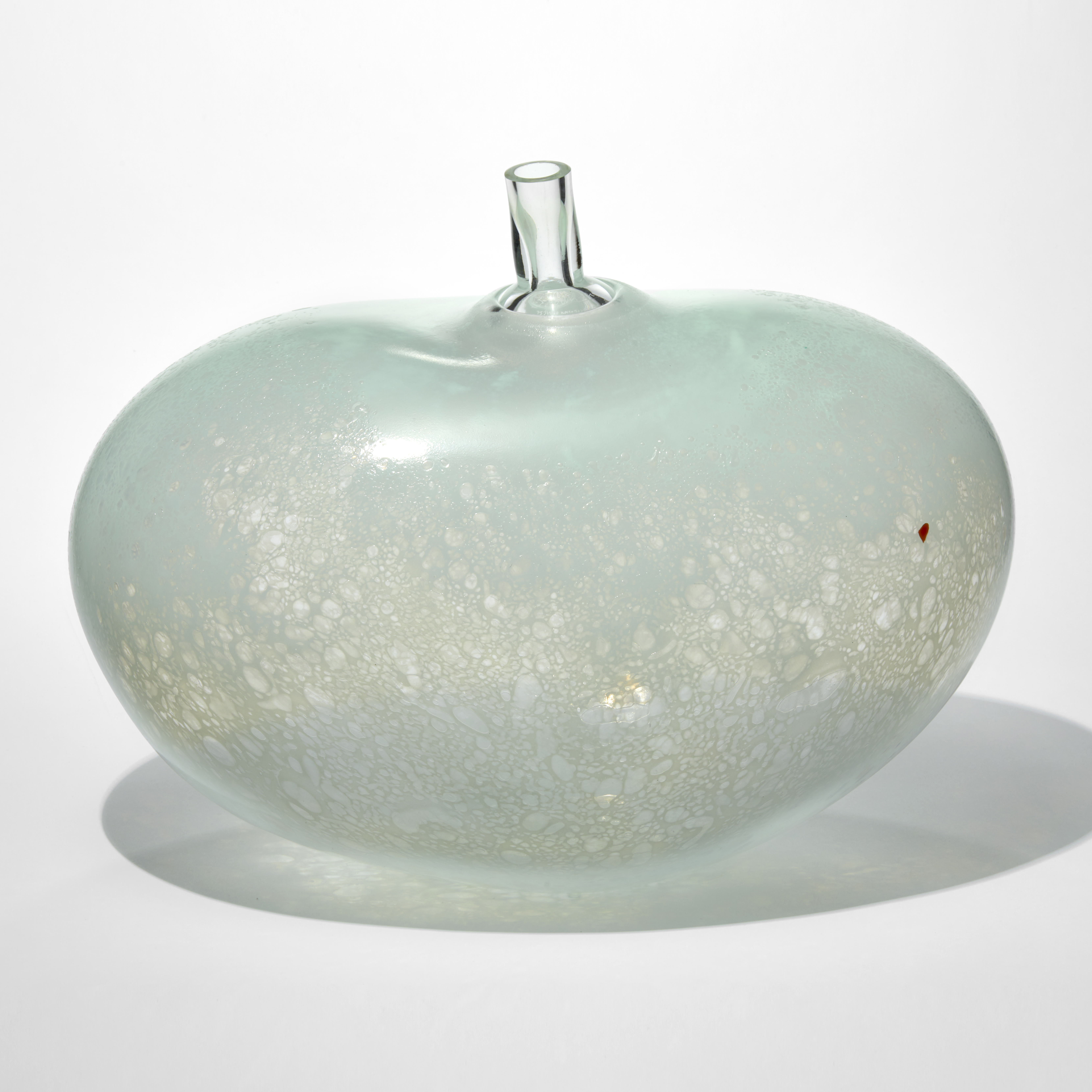 rounded bean shaped vessel in transparent and mottled soft celadon jade with a red beauty mark and short clear tubular stem on the top hand made from glass