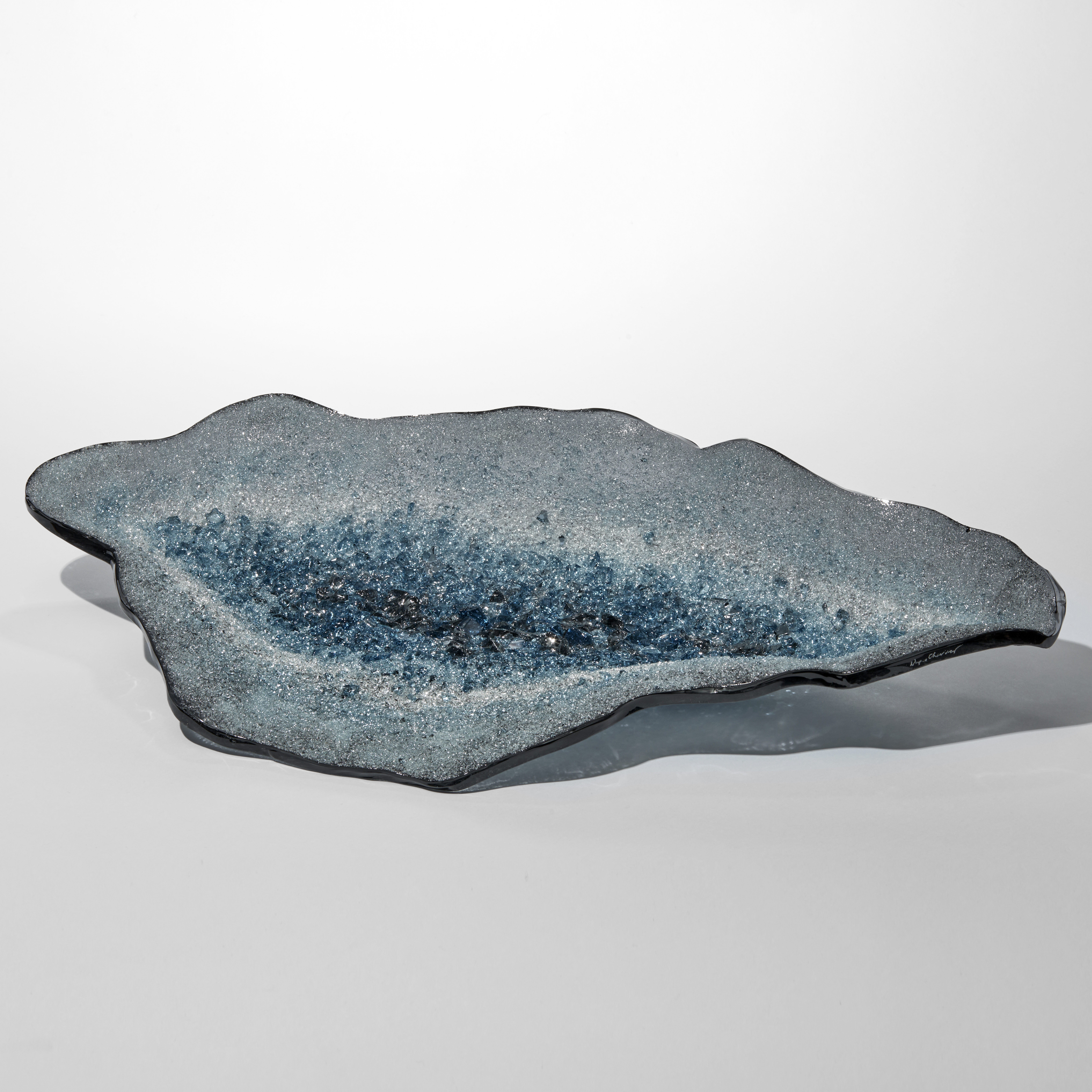 angular oyster shell prone centrepiece with dark grey rim and the interior filled with tiny twinkling shards in grey white and rich aqua blue in the centre hand made from glass