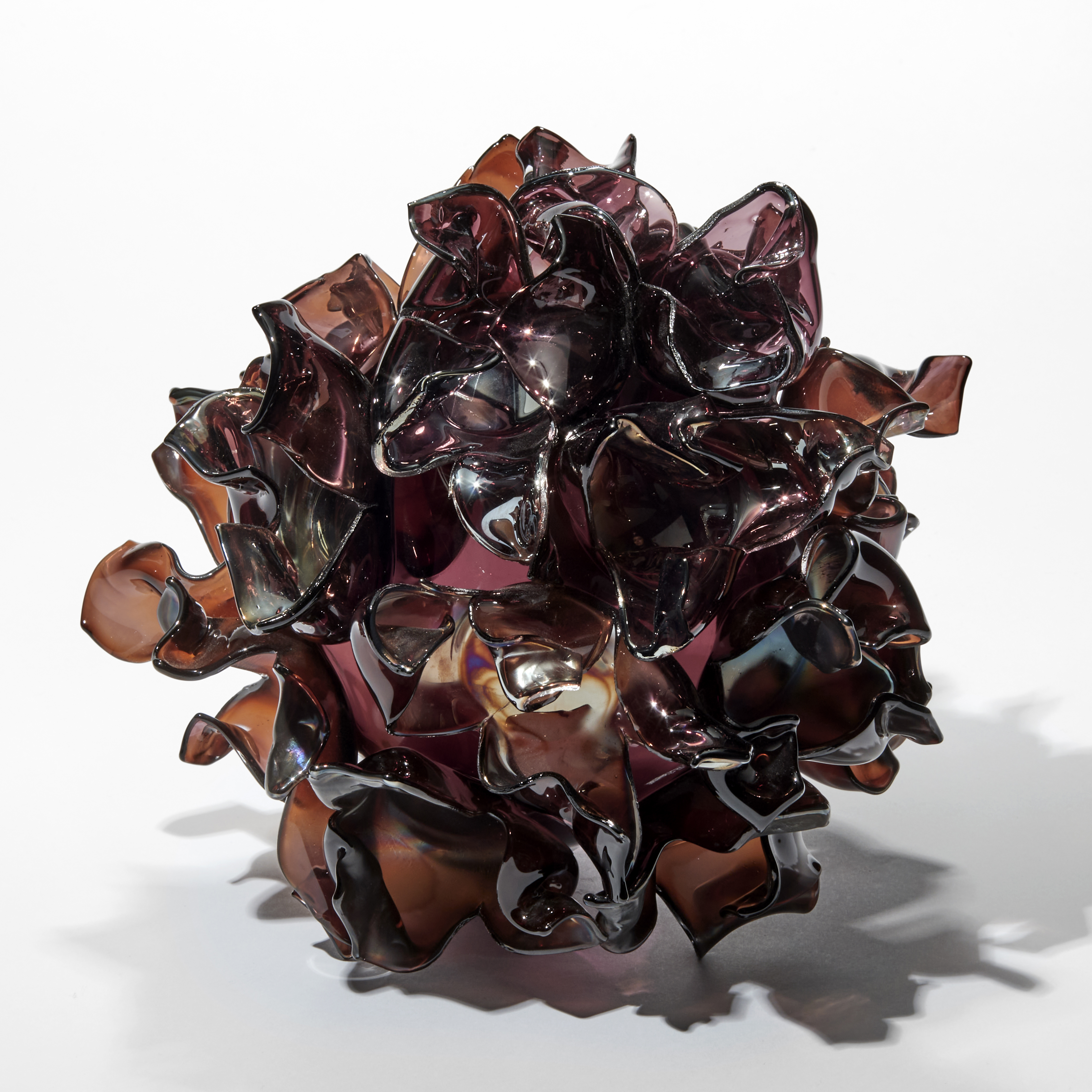 round transparent aubergine and tobacco coloured ball covered in scrunched petal shapes each with a soft iridescent colouring on the surface handmade from glass