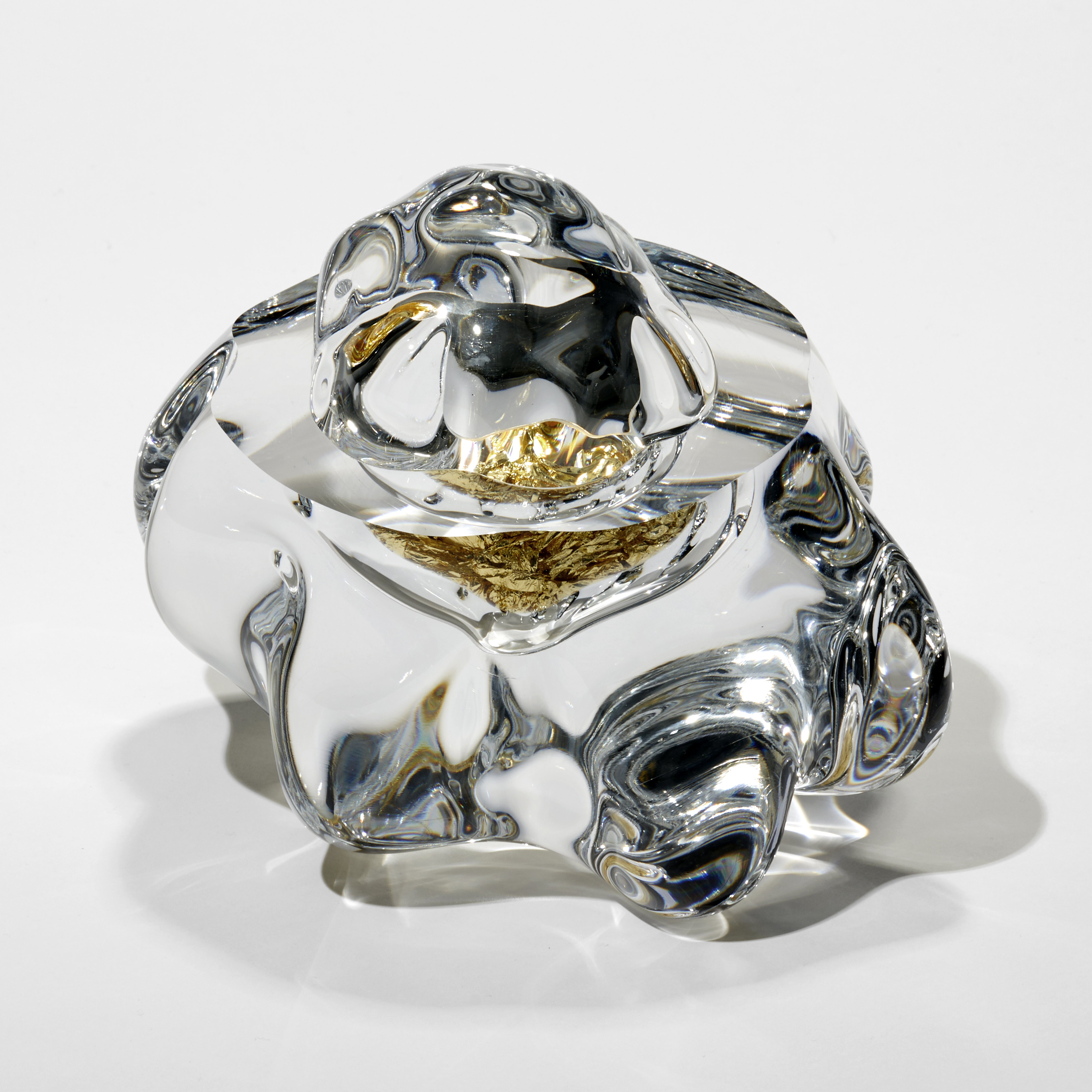 amorphous clear mass with flat top surface and uneven clear domed lid bonded on place with the middle filled with crushed gold leaf hand blown from glass