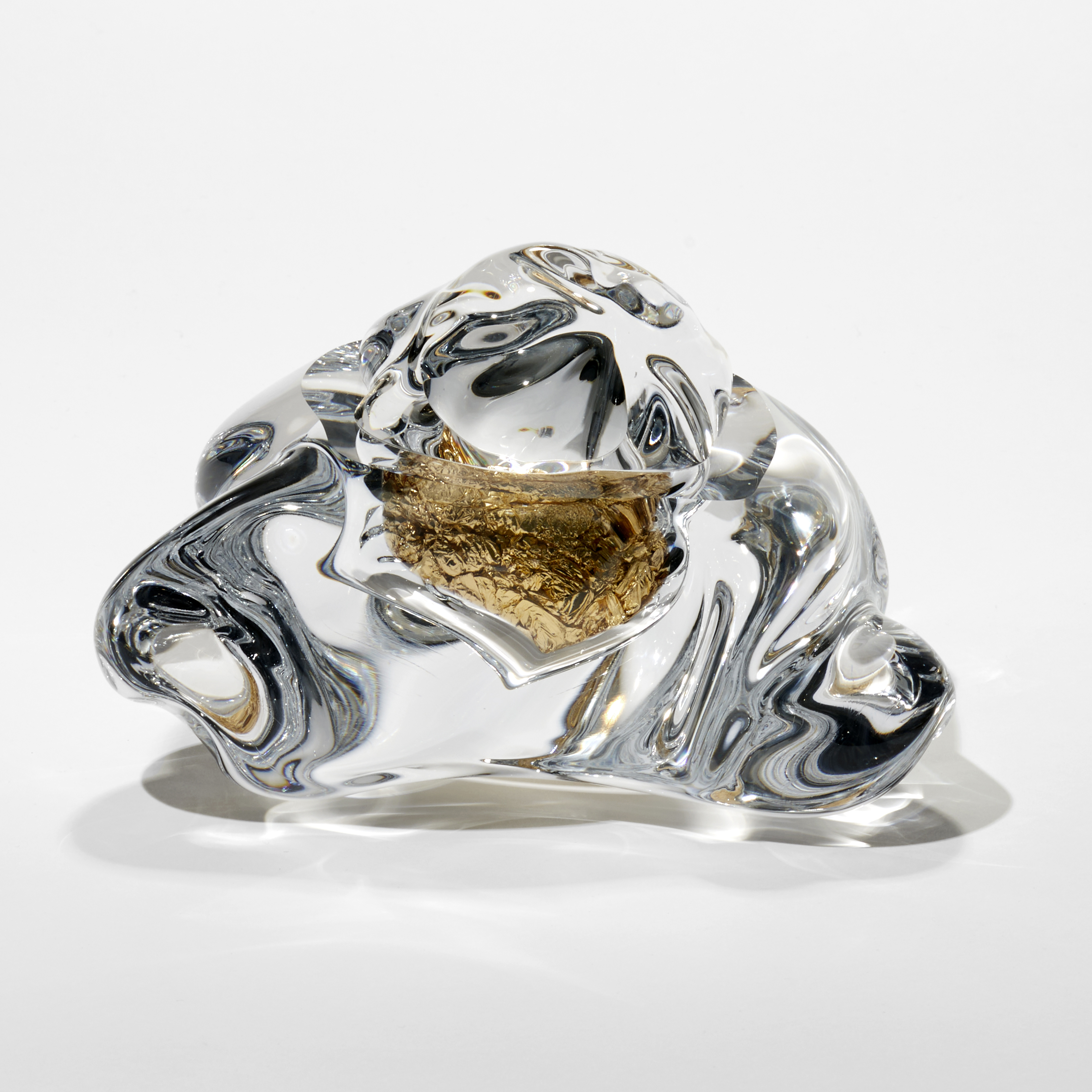 clear amorphic soft mass with a central cavity filled with crushed gold leaf hand made from blown and but glass with 23 carat red gold leaf