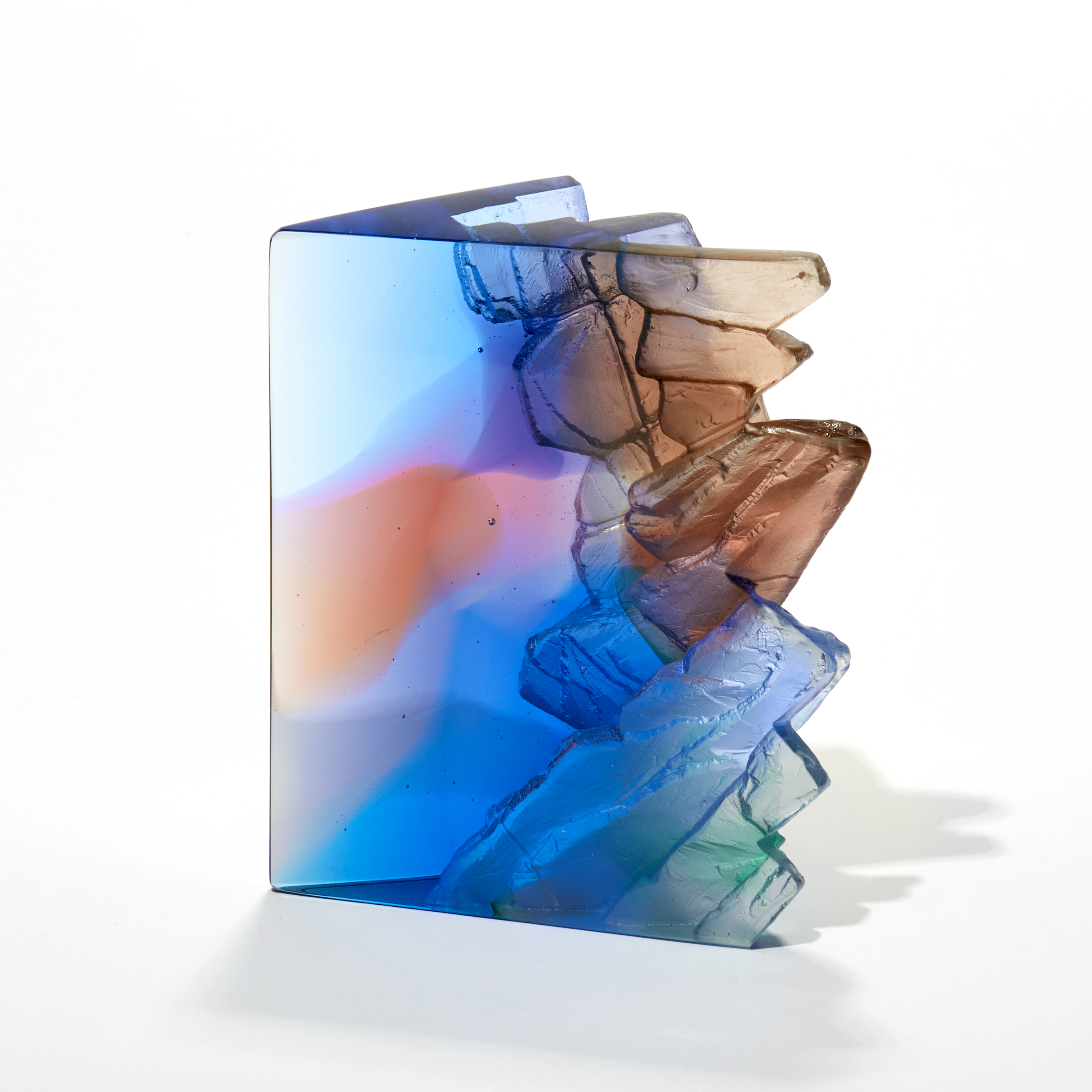 cliff and landscape inspired artwork in transparent blues pink peaches jade and aubergine with two vertical glossy sides and top and one side with a craggy cliff edge like texture hand made from cast glass