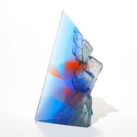 transparent tall offset pyramid in rich blue with hazy areas of salmon pinky red with two sides polished flat and two sizes inverted with craggy textures hand made from cast glass