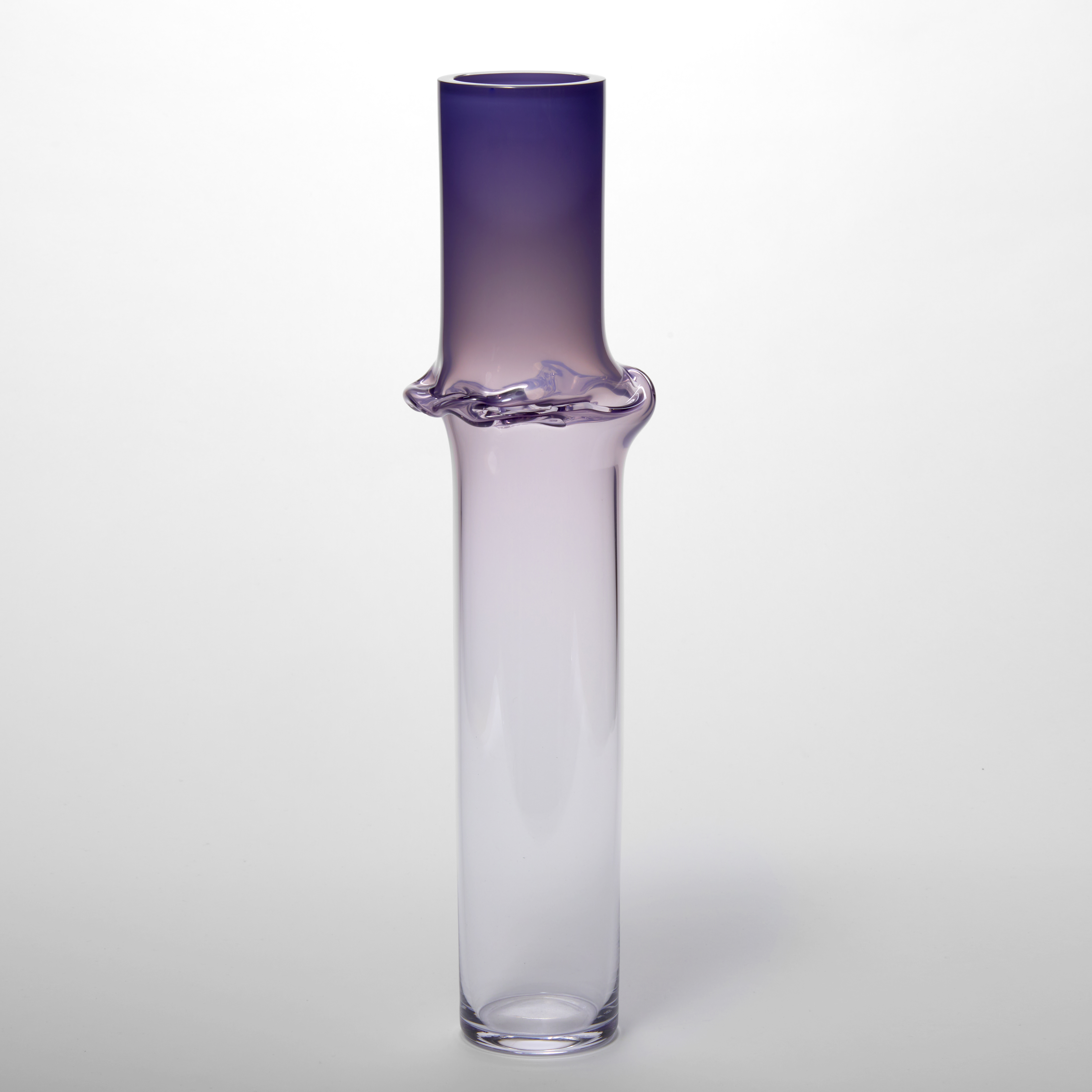 tall cylindrical vessel with a rich purple top half fading to clear with a creased undulating raised circumference line a third from the top hand made from glass