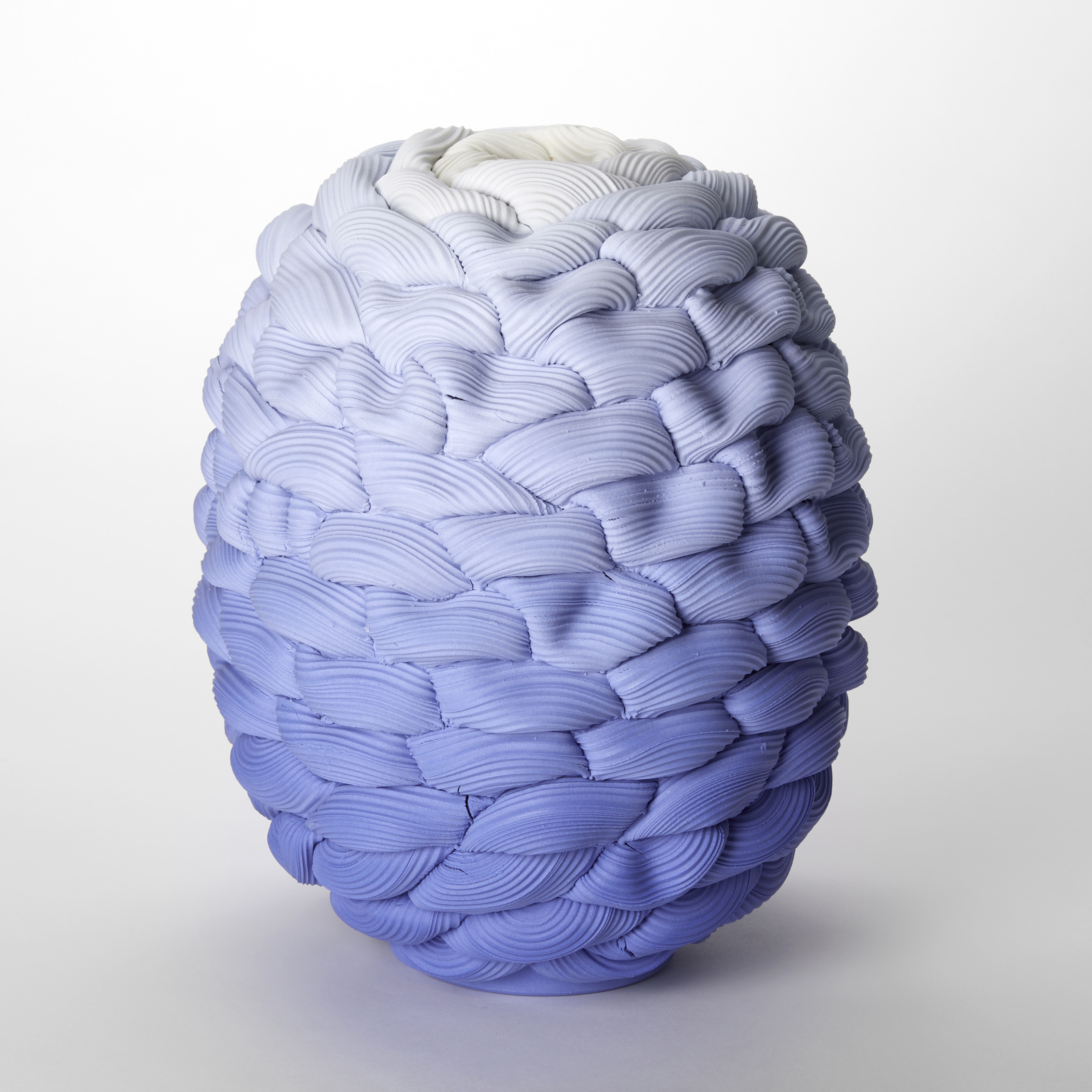 round squat barrel shaped vase with small opening at the top created from stacked interwoven ridged rings fading from dark intense blue at the base through to white at the top hand made and thrown from parian porcelain