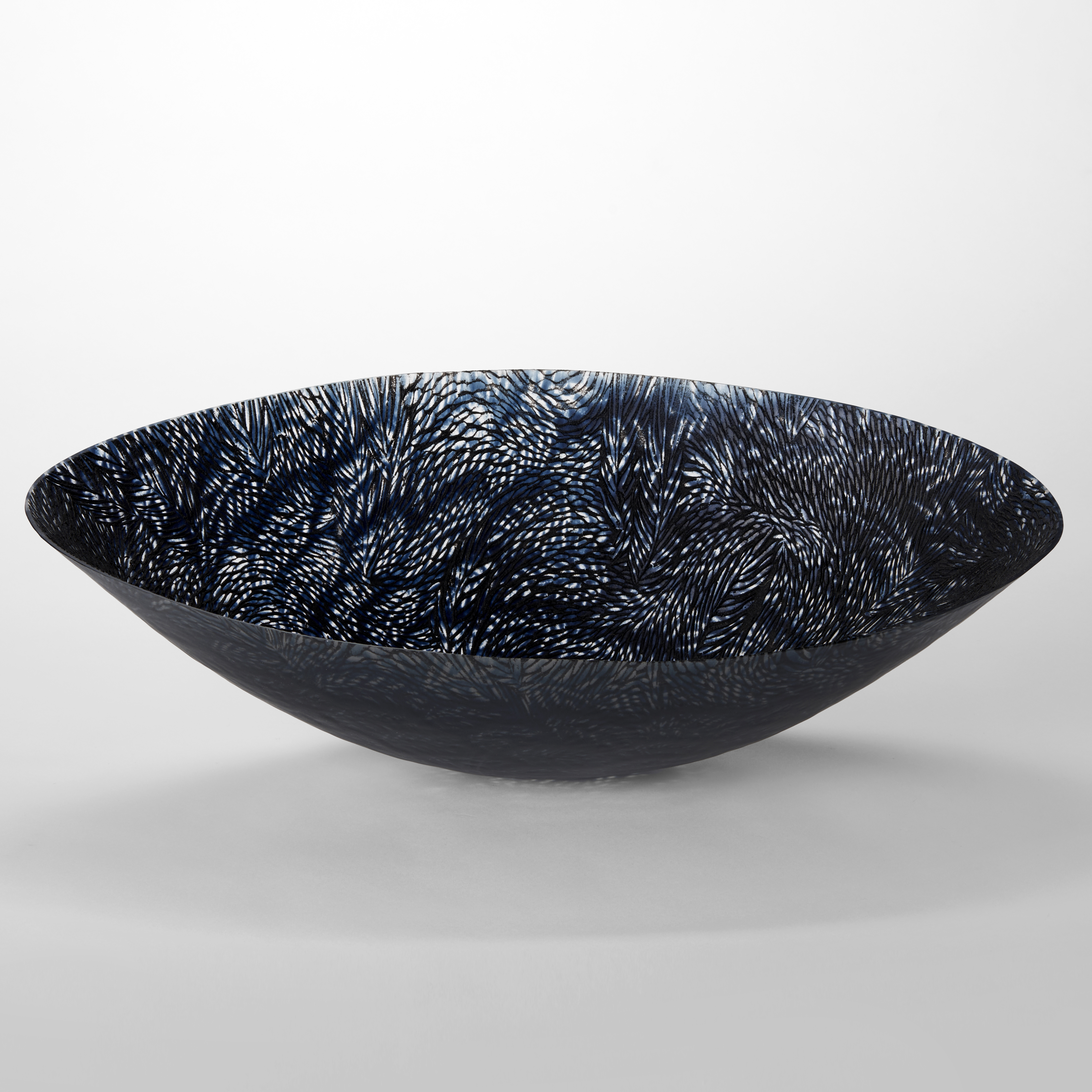 translucent black light grey and dark blue oval bowl perched on a small rounded base with sweeping sides and a fine organic texture moving over the surface resembling ears of corn hand made from glass