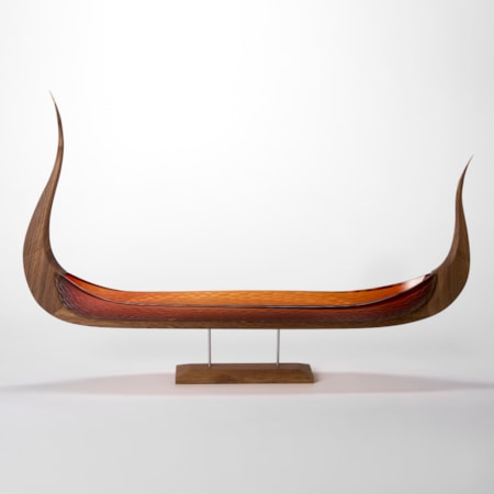 simple and stylish artwork based on a viking ship with keel made of fumed oak and hull of red orange blown glass with a repeat pattern cut into the surface displayed raised on a simple stand