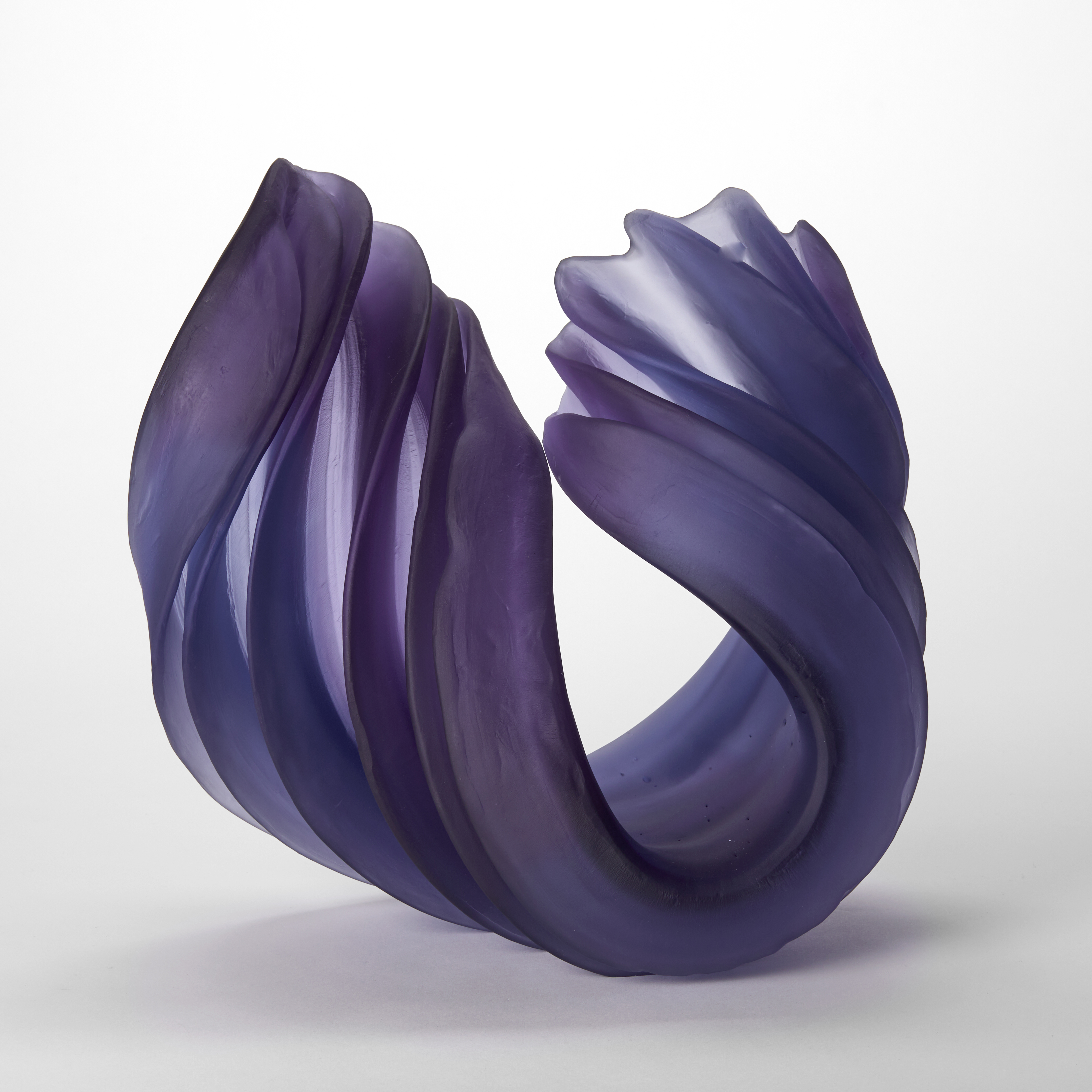 a purple curled ridged and folded form with a round base and trailing upward ends with the appearance of chiffon or ribbon with transparent see through sections yet also heavy and weighted hand made from glass