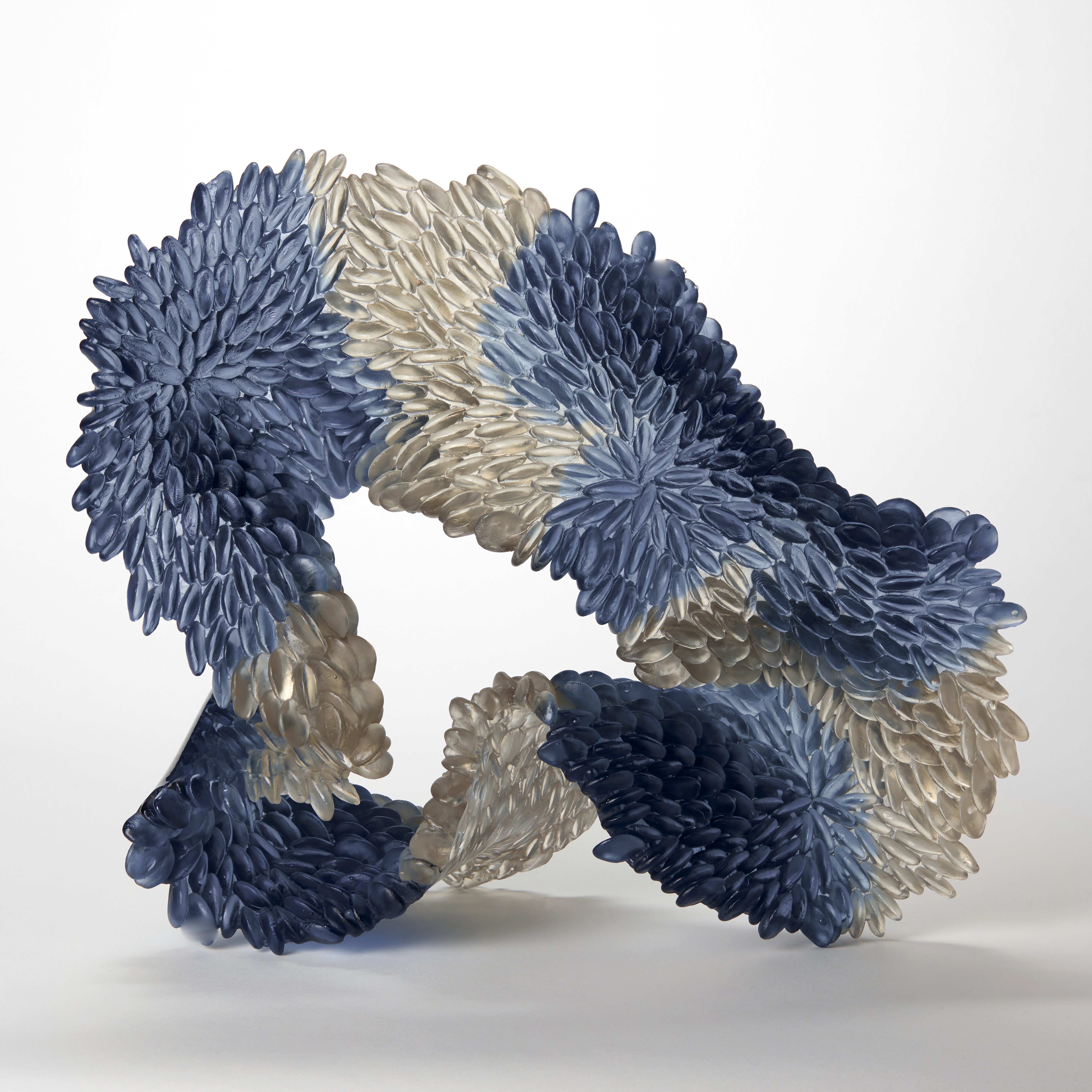 indigo rich blue and soft silvery grey standing textured organic shaped looped sculpture with scaly raised texture one side and shiny and flat on the other hand made from cast and shaped glass